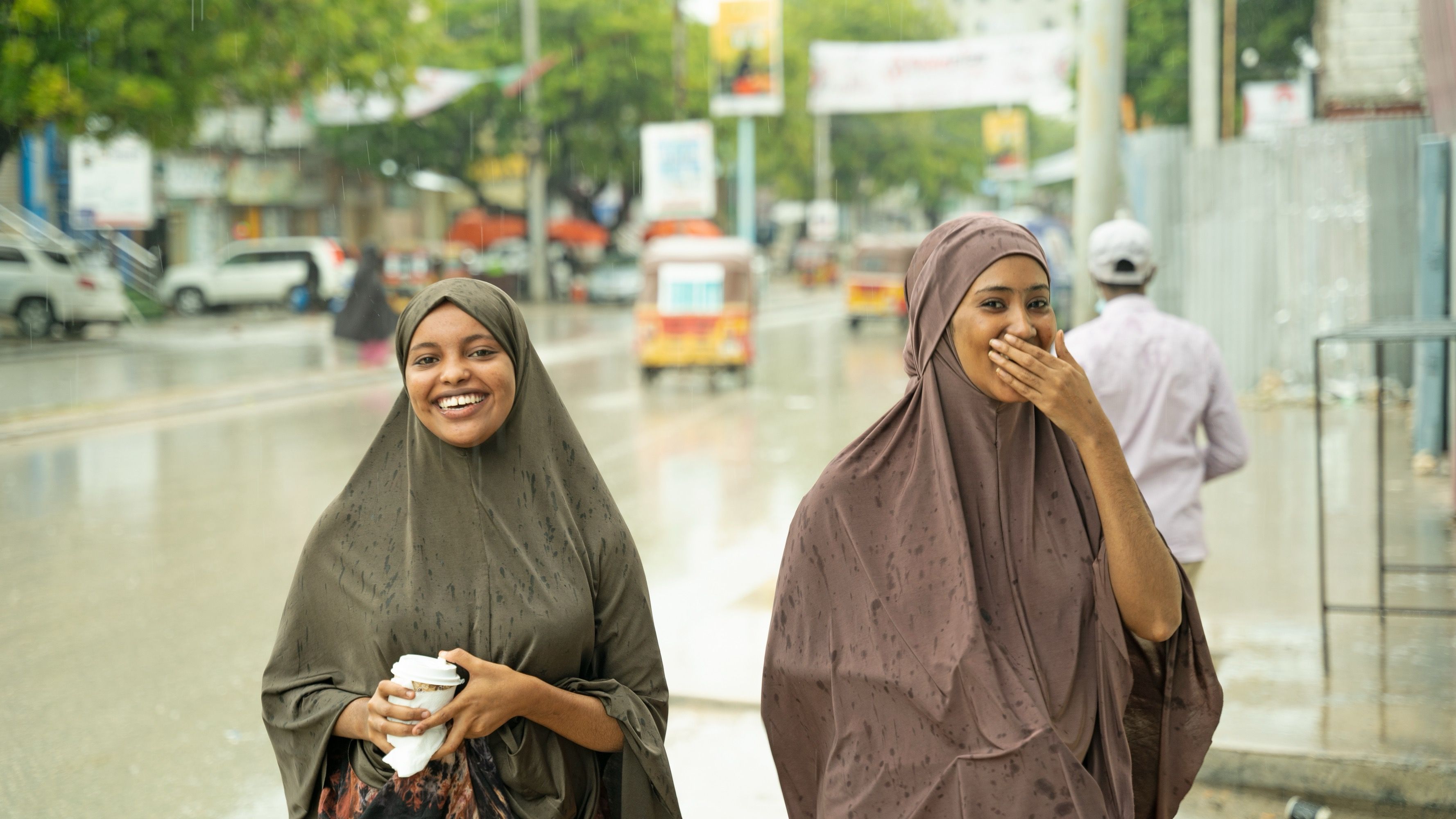 Two women smiling and looking at the camera standing outside on a rainy day