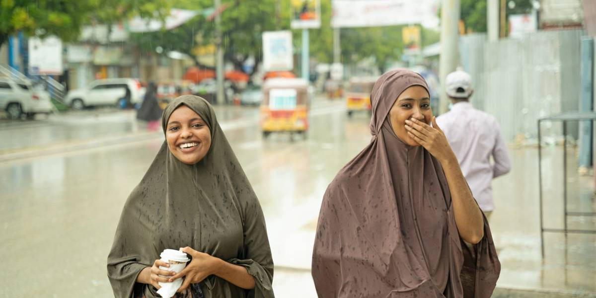 Two women smiling and looking at the camera standing outside on a rainy day