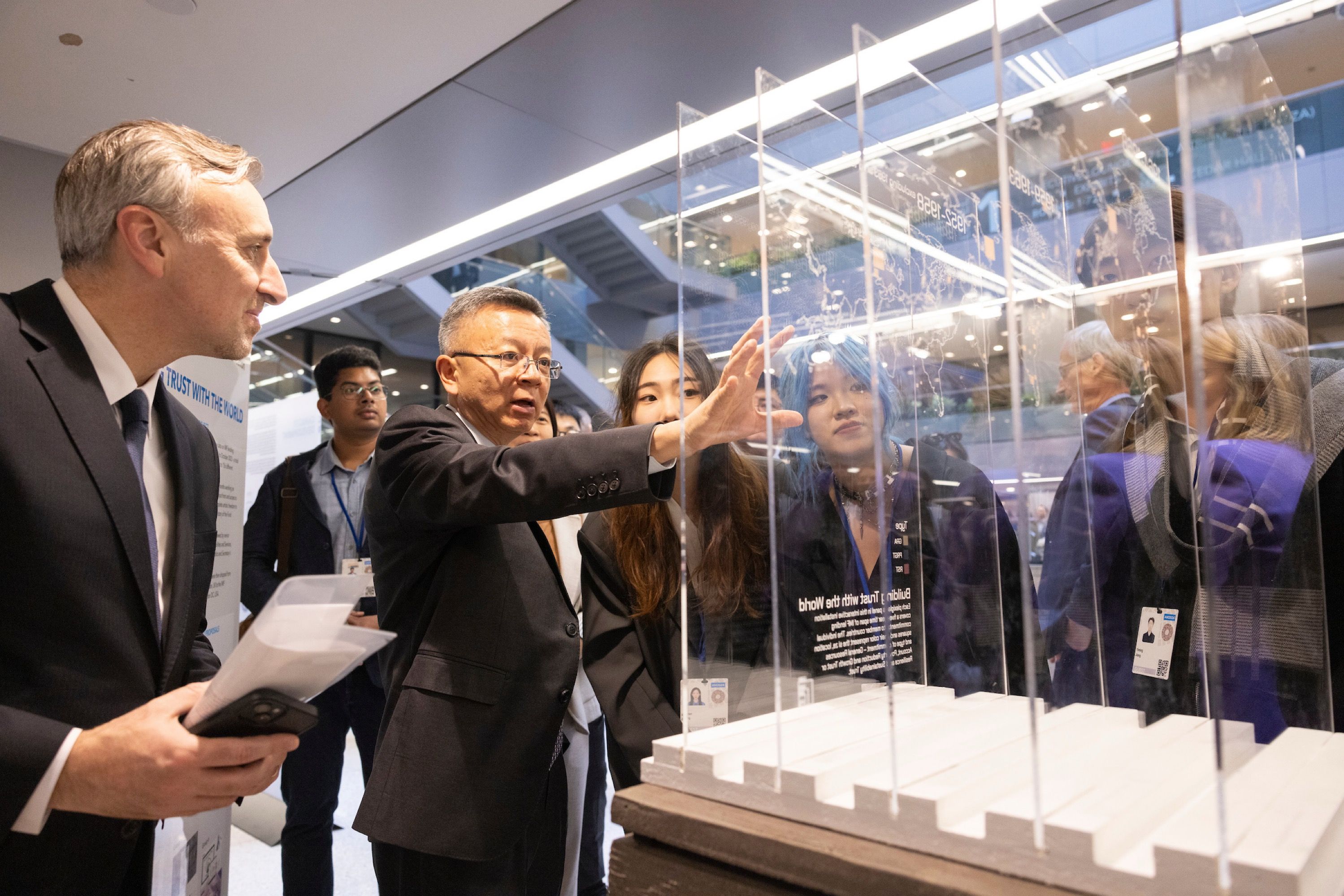 Bo Li speaking in front of a glass exhibit with several people looking at the exhibit.