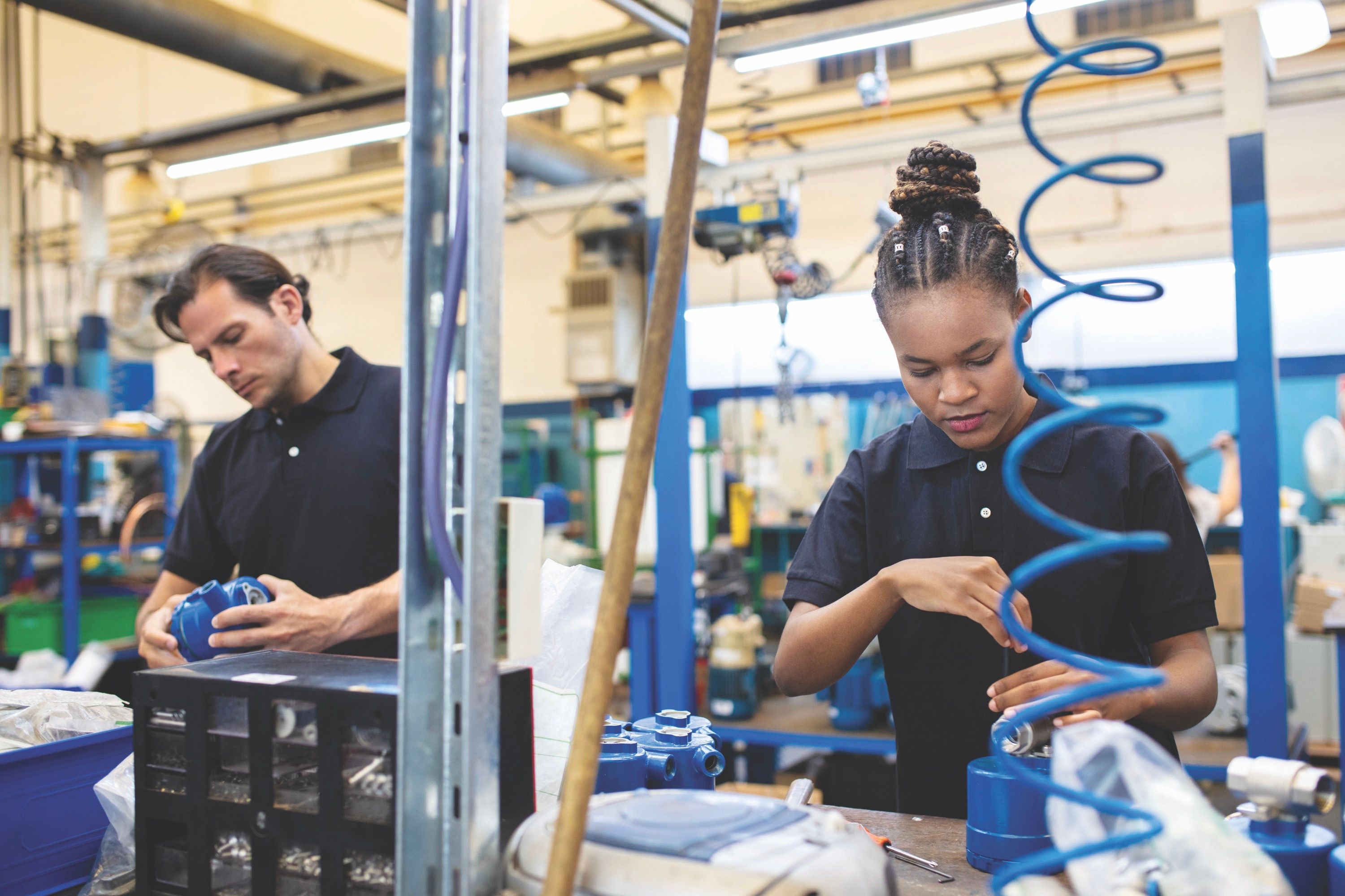 A man and woman dressed in navy blue polos work in a factory setting