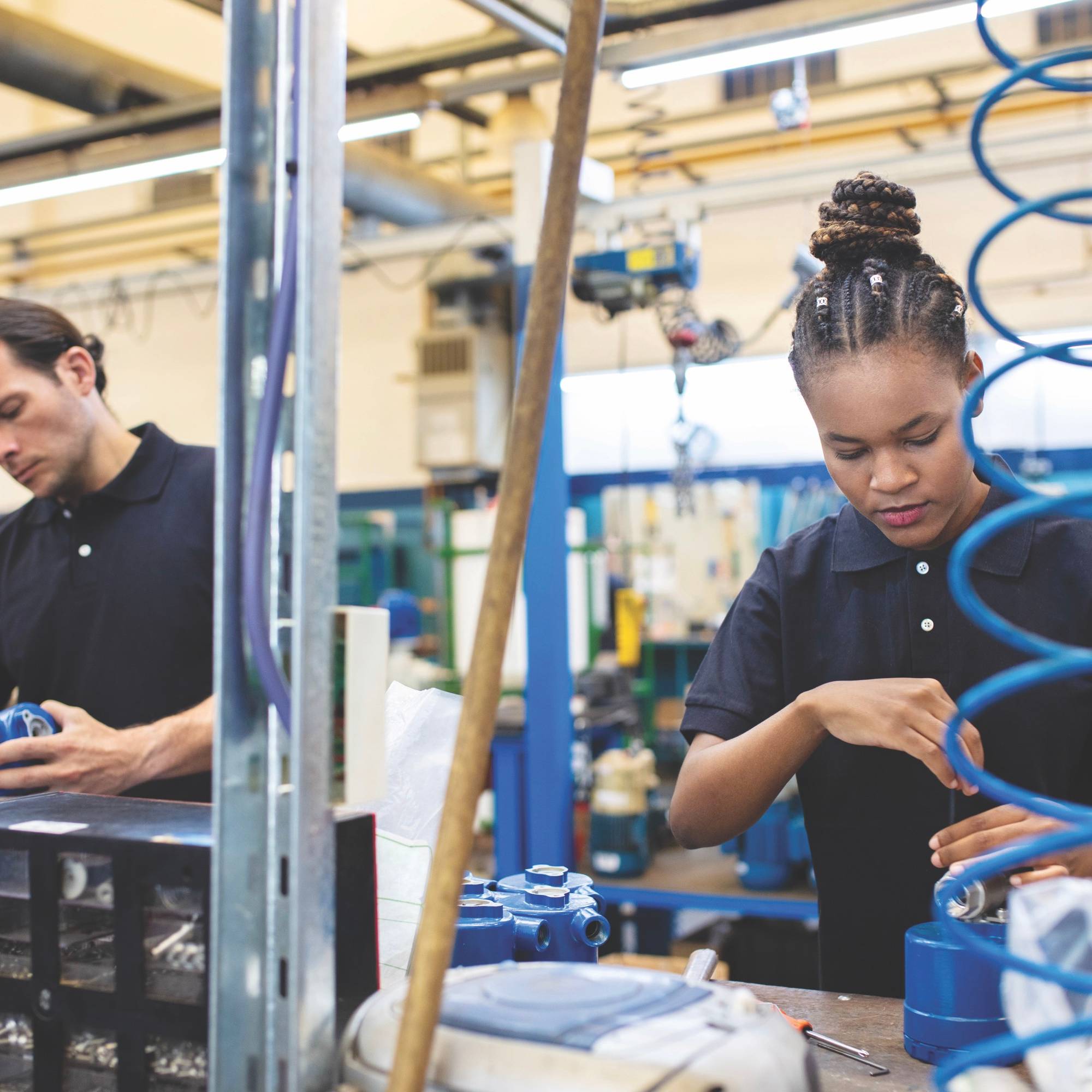 A man and woman dressed in navy blue polos work in a factory setting