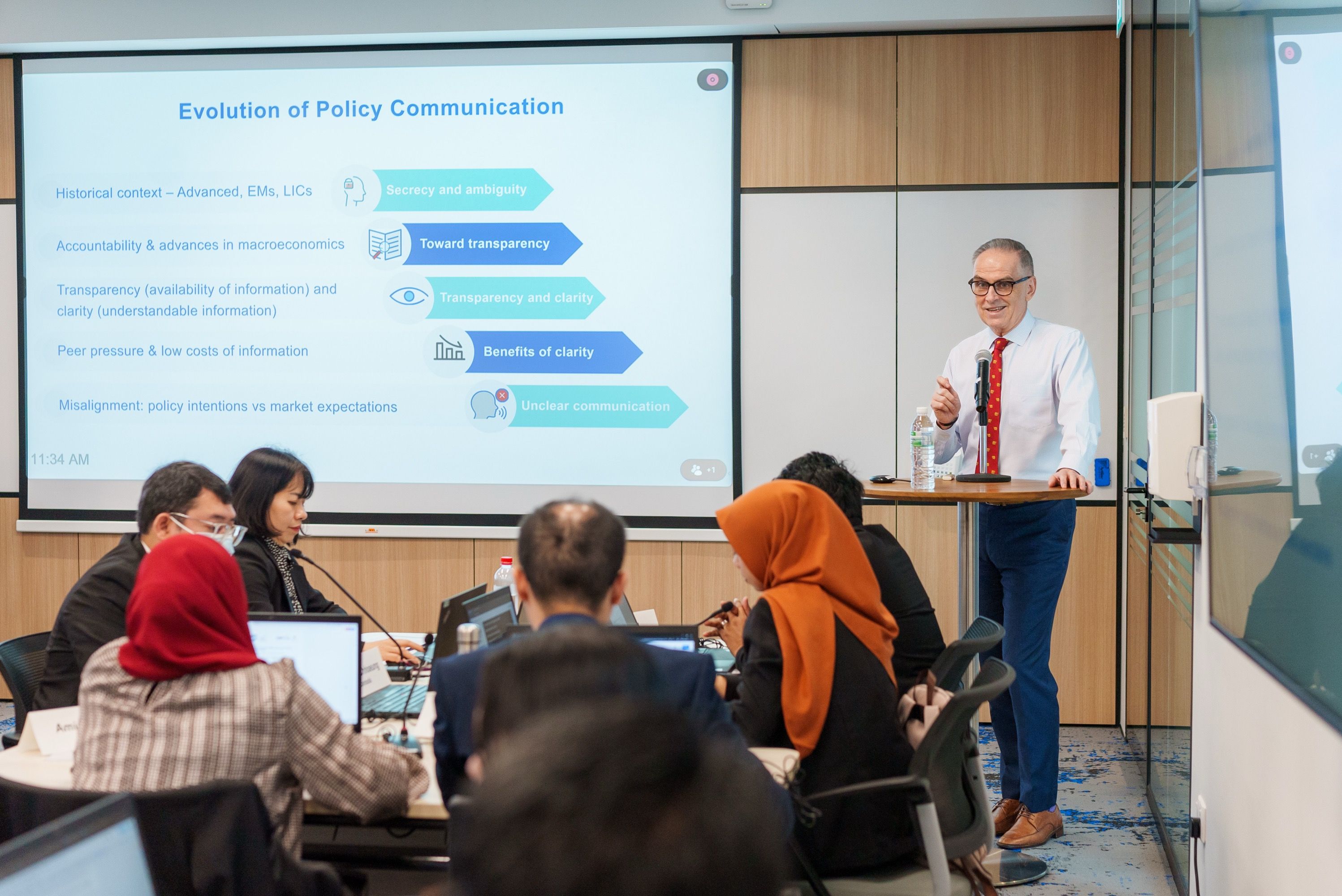 A man standing at a table speaking to a diverse group of people