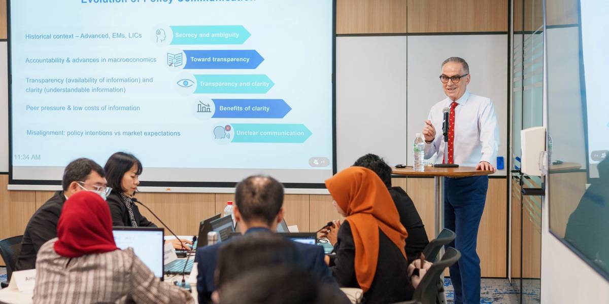 A man standing at a table speaking to a diverse group of people