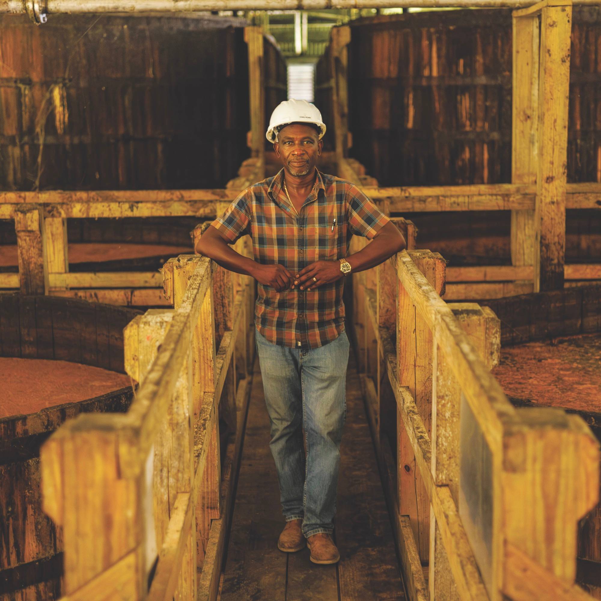 A man stands next to large wooden barrels, smiling and looking out at the camera.