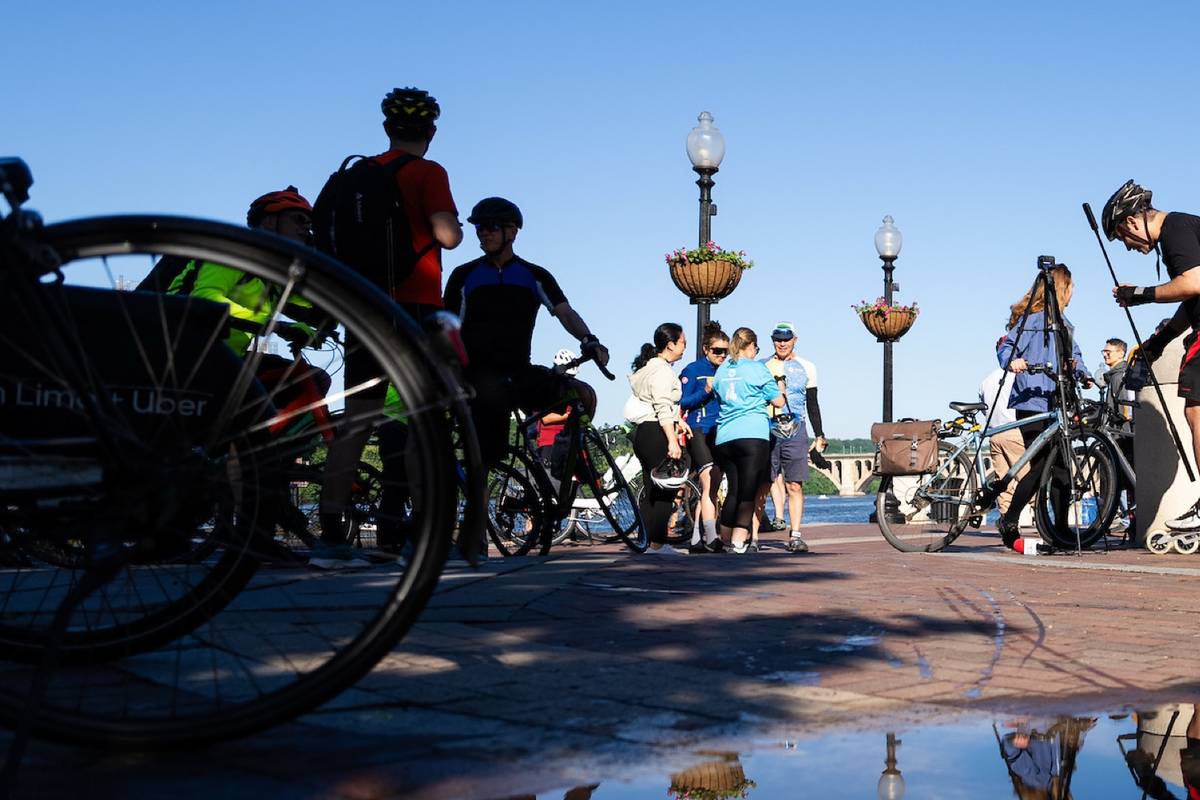 A puddle in the foreground reflecting a daytime scene with bikes, a group of people and a man on rollerblades.