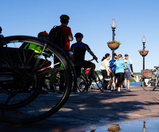 A puddle in the foreground reflecting a daytime scene with bikes, a group of people and a man on rollerblades.