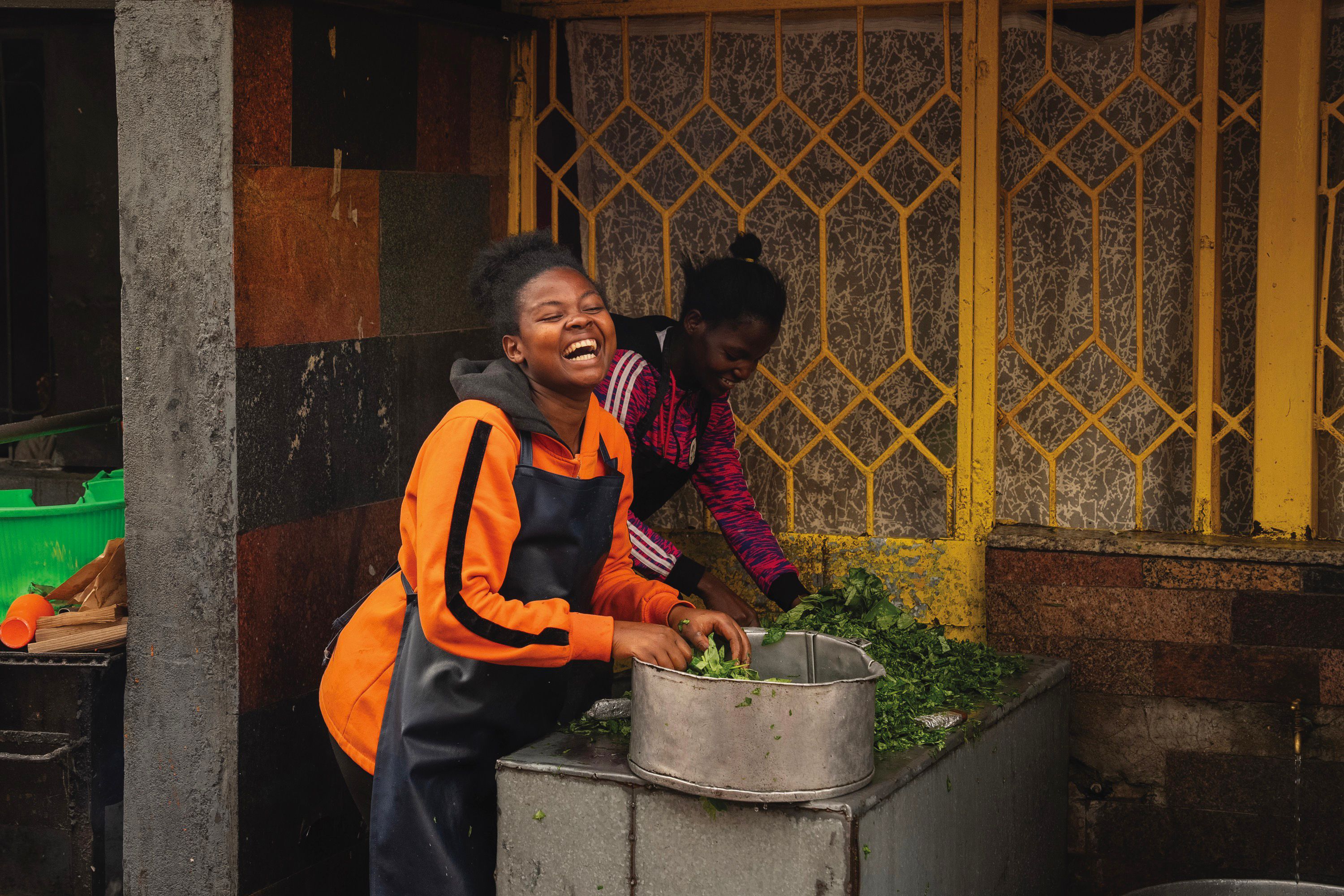 A woman is smiling and laughing as she is holding green plants inside of a metal container