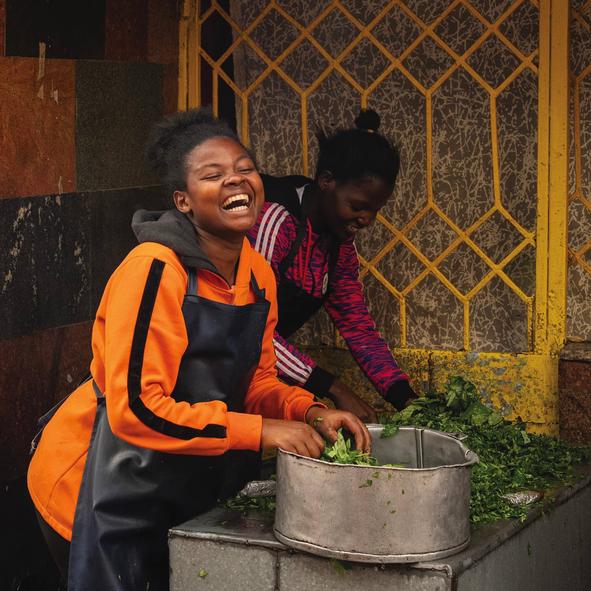 A woman is smiling and laughing as she is holding green plants inside of a metal container