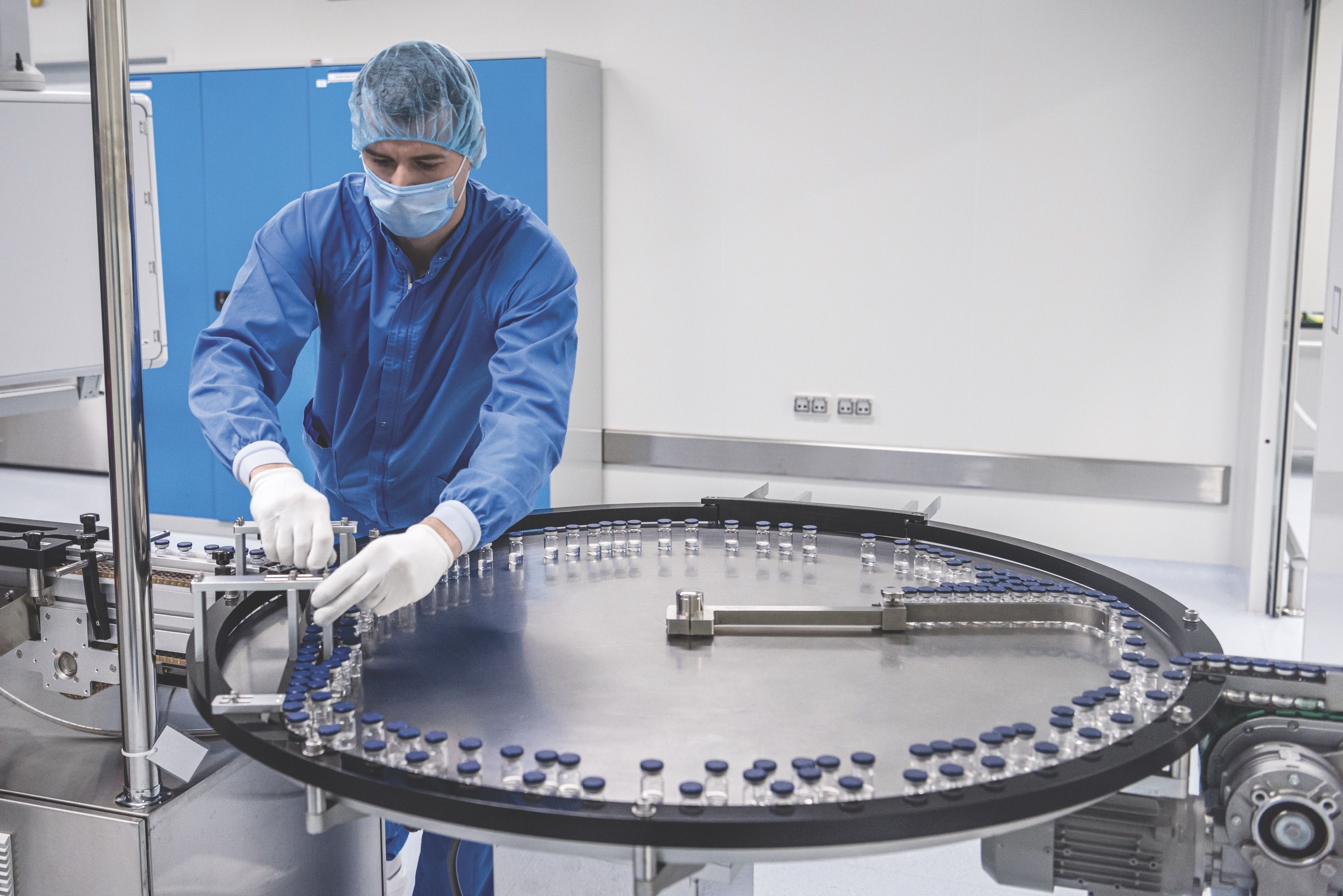 A man wearing a blue uniform is engaged in working on a machine, demonstrating technical skills in a factory environment.