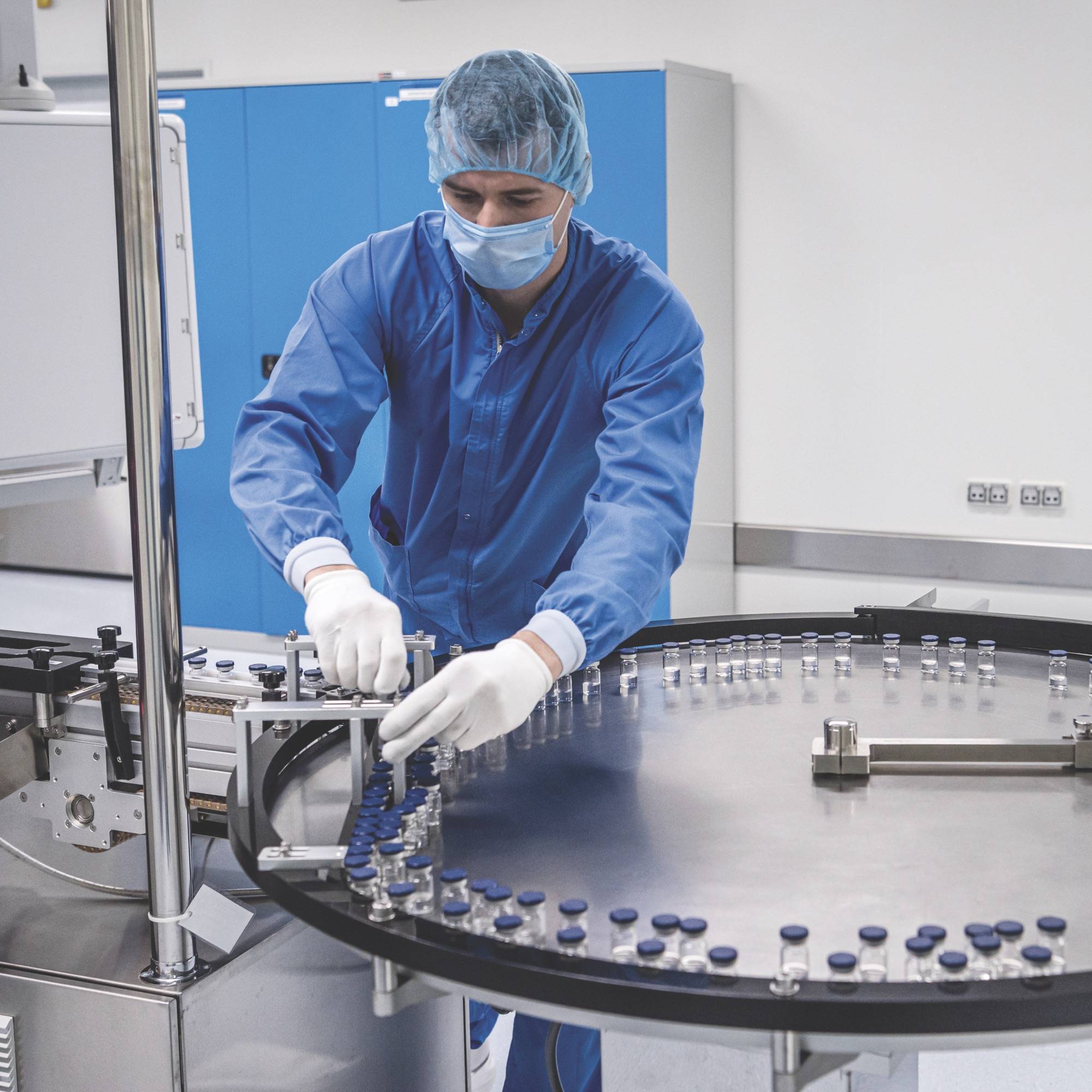 A man wearing a blue uniform is engaged in working on a machine, demonstrating technical skills in a factory environment.