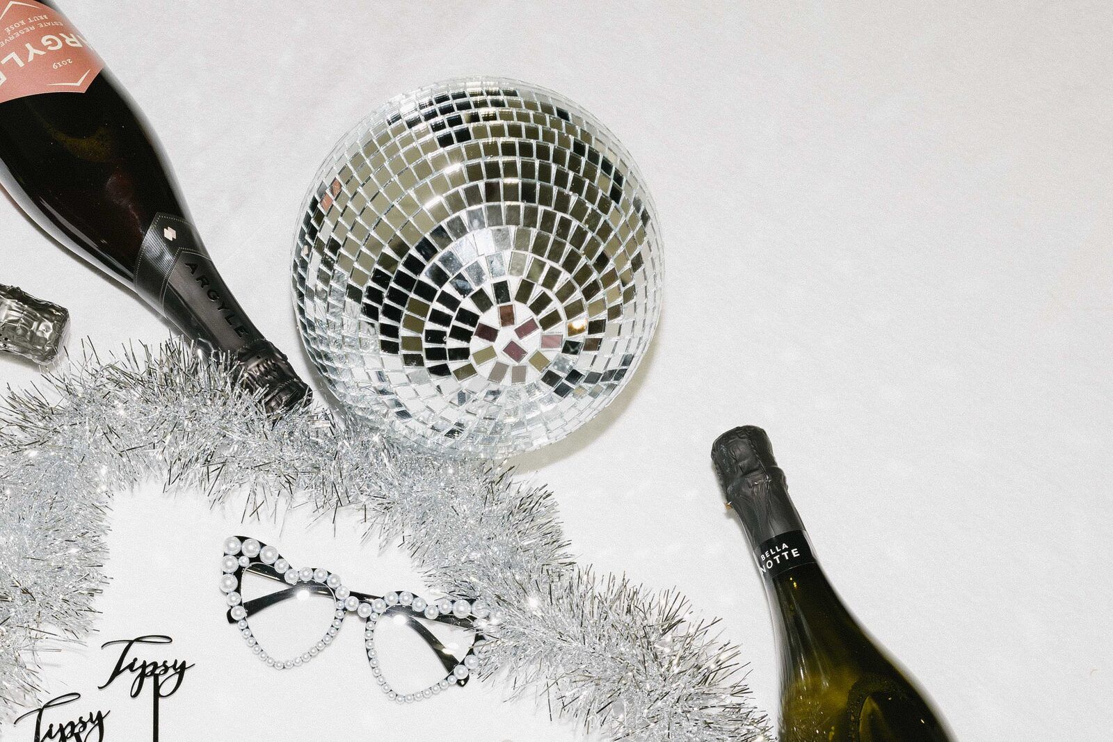 Styled detail flat-lay with a disco ball, champagne bottles, and party glasses
