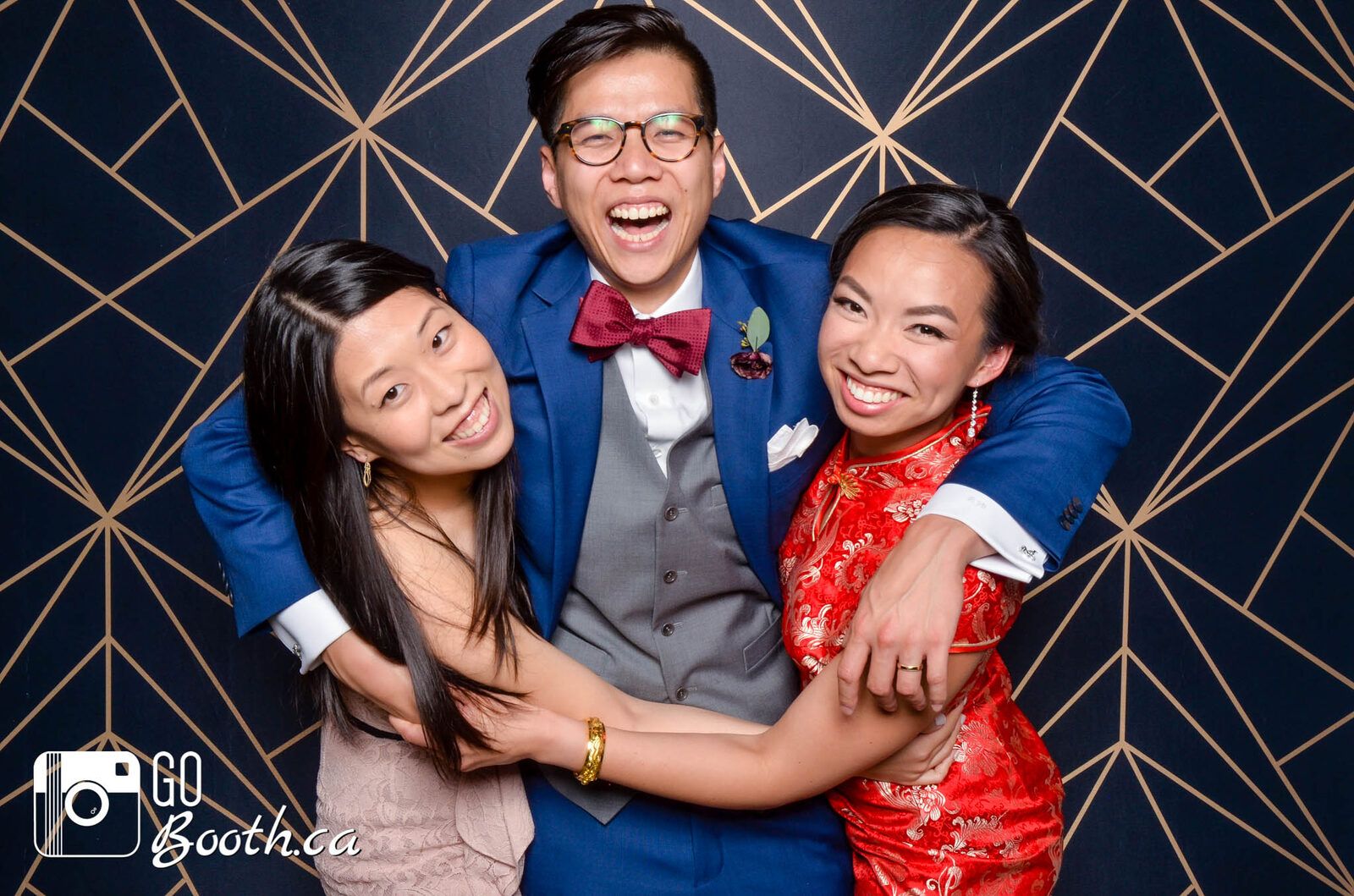 Three friends embracing in front of a navy and copper geometric backdrop
