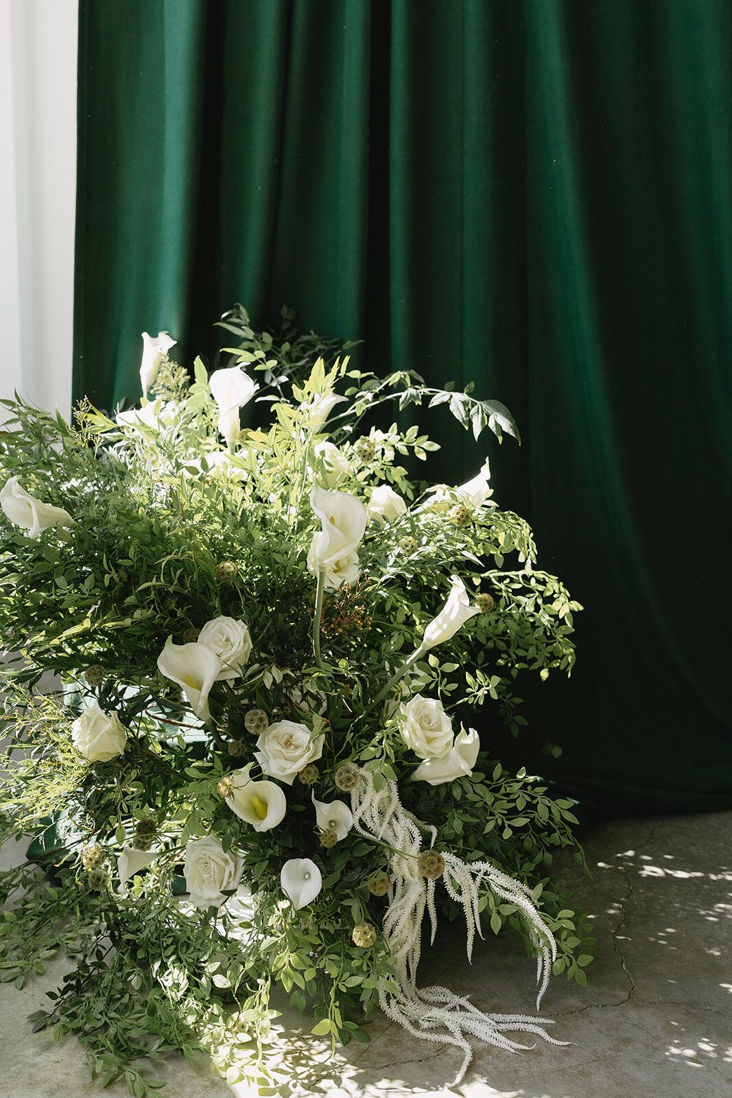 White florals arranged in front of an emerald velour backdrop