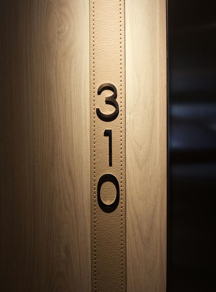Numéro de chambre 310 en chiffres métalliques noirs sur une bande de cuir beige surpiqué (photo Unsplash provisoire)