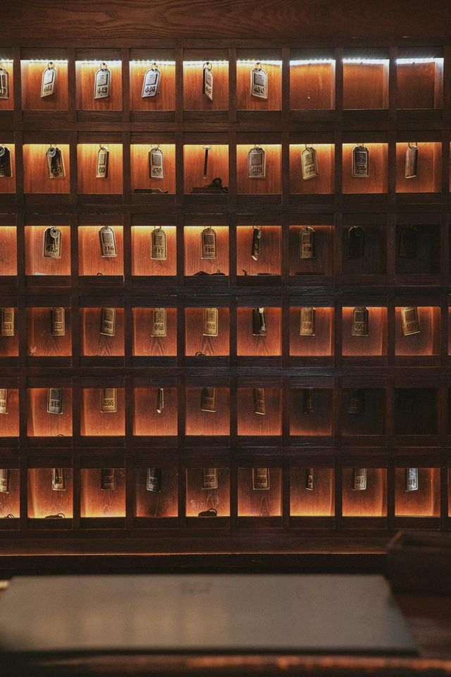 Casiers en bois éclairés contenant les clés des chambres derrière le comptoir d'un hôtel (photo Unsplash provisoire)