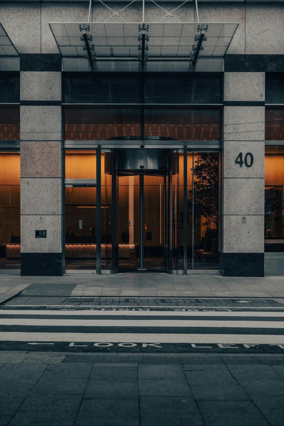 Entrée d'un immeuble moderne avec porte tambour vitrée, hall éclairé et numéro 40 sur la façade en pierre (photo Unsplash provisoire)
