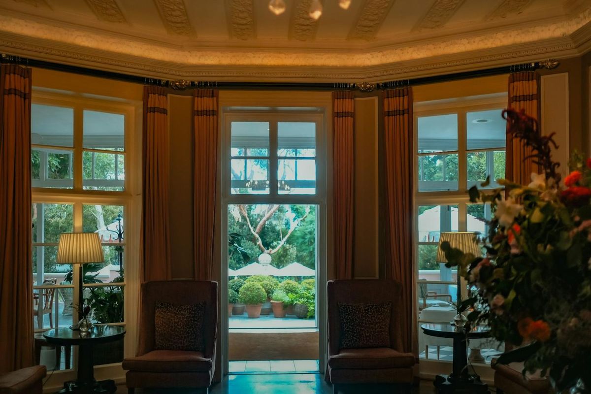 Salon d'hôtel élégant avec fauteuils, lampes et grandes portes-fenêtres ouvrant sur un jardin (photo Unsplash provisoire)