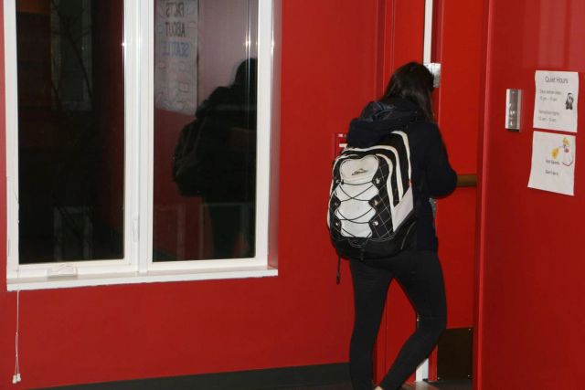 Étudiante de dos avec un sac à dos, ouvrant la porte rouge d'une résidence (photo Unsplash provisoire)