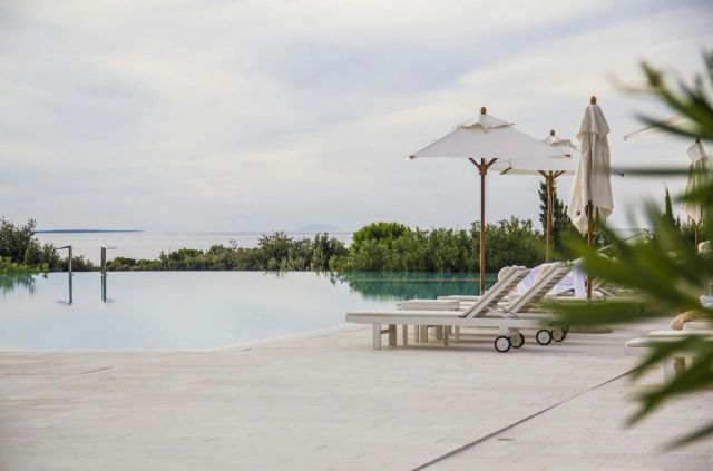 Piscine à débordement d'un lieu de vacances avec transats et parasols blancs face à la mer (photo Unsplash provisoire)