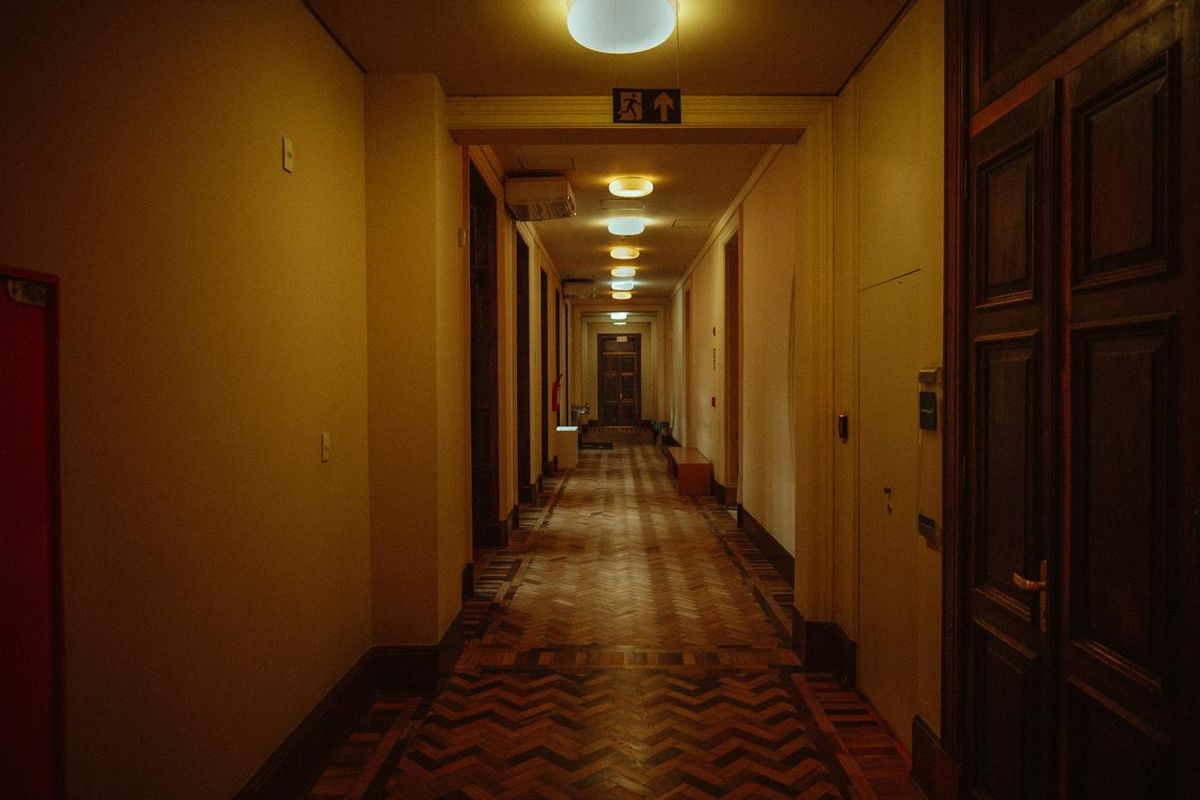 Long couloir d'hôtel feutré à la lumière chaude, parquet à chevrons et portes de chambres en bois sombre (photo Unsplash provisoire)