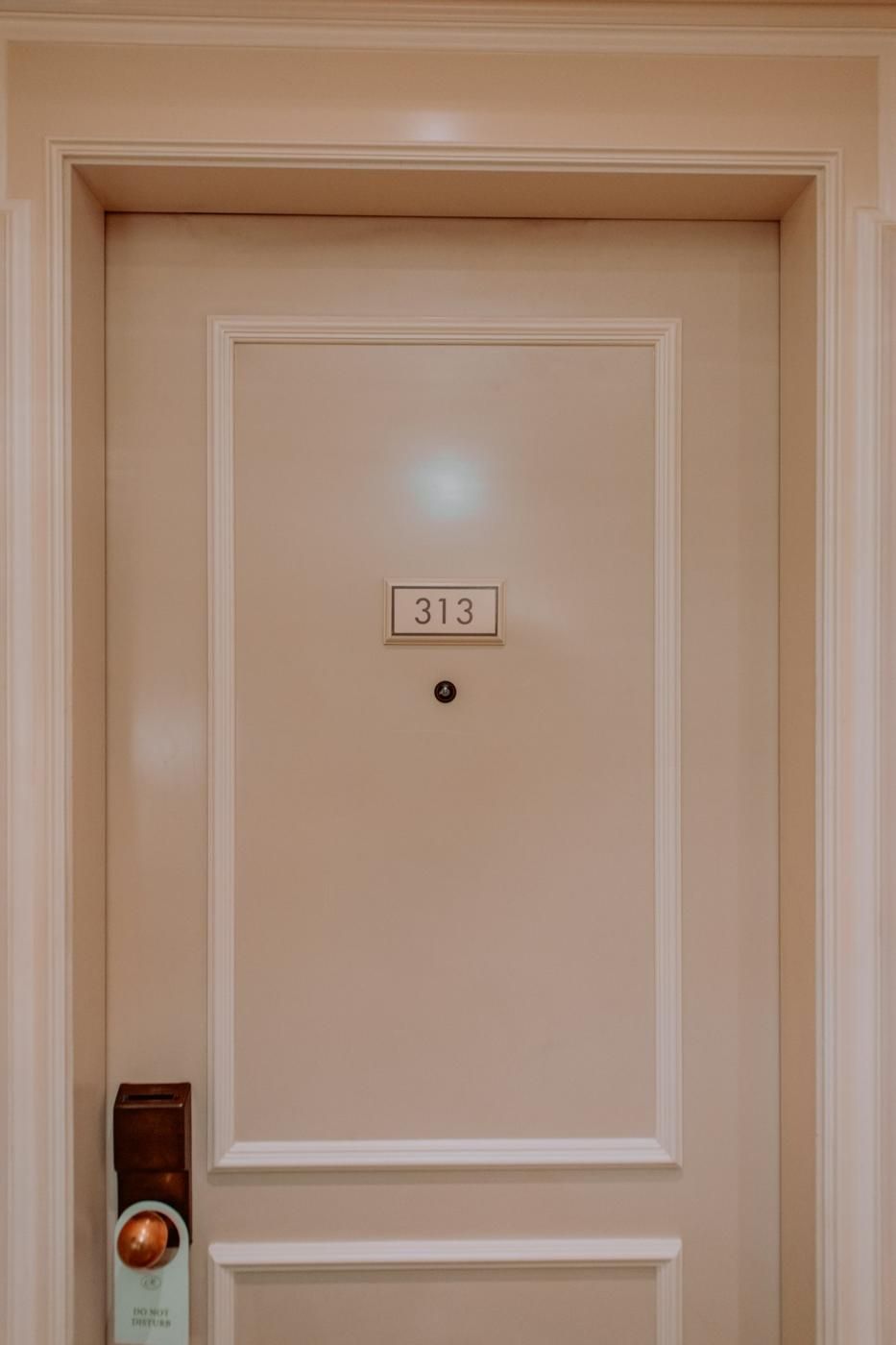 Porte de chambre d'hôtel crème ornée d'une plaque numéro 313, avec serrure électronique à carte (photo Unsplash provisoire)