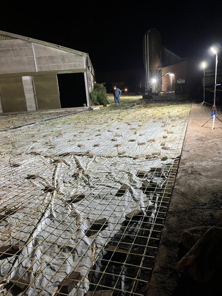 Glass-fibre mesh on spacers across a livestock-barn floor at night, with the shed and silo behind