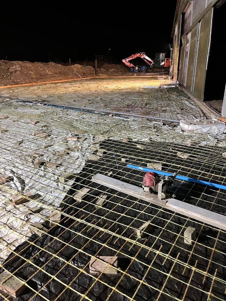Livestock-barn floor with glass-fibre mesh, a screed rail and site lighting before the pour