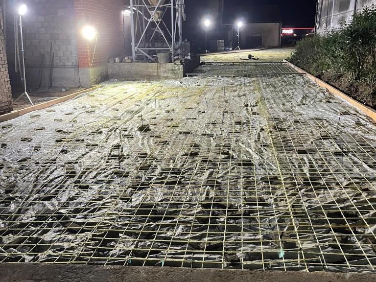 Livestock-barn floor reinforced with glass-fibre mesh before the pour, beside the silo and the sheds