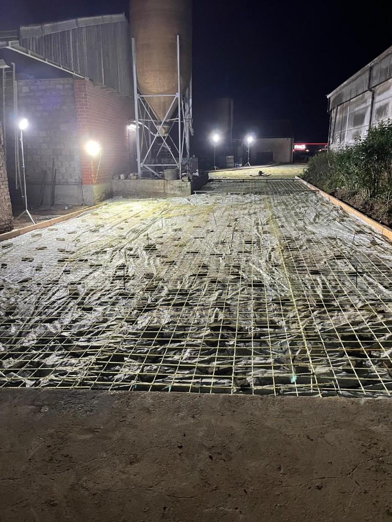 Livestock-barn floor reinforced with glass-fibre mesh before the pour, beside the silo and the sheds