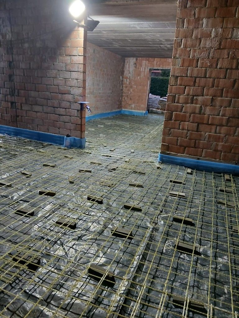 Yellow glass-fibre mesh on spacers over a vapour barrier in a residential room with brick walls