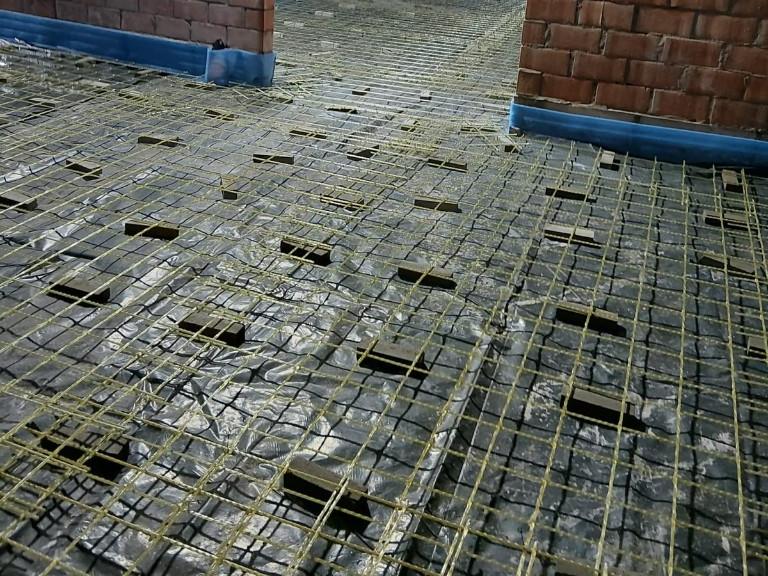Yellow glass-fibre mesh on spacers over a vapour barrier in a residential room with brick walls