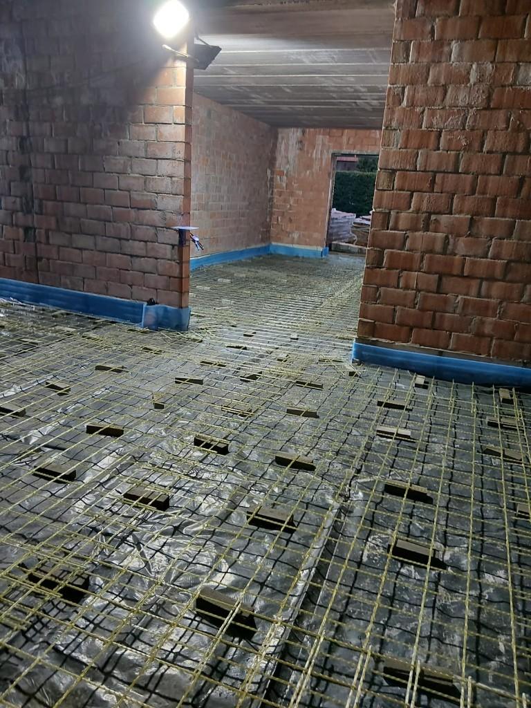 Yellow glass-fibre mesh on spacers over a vapour barrier in a residential room with brick walls