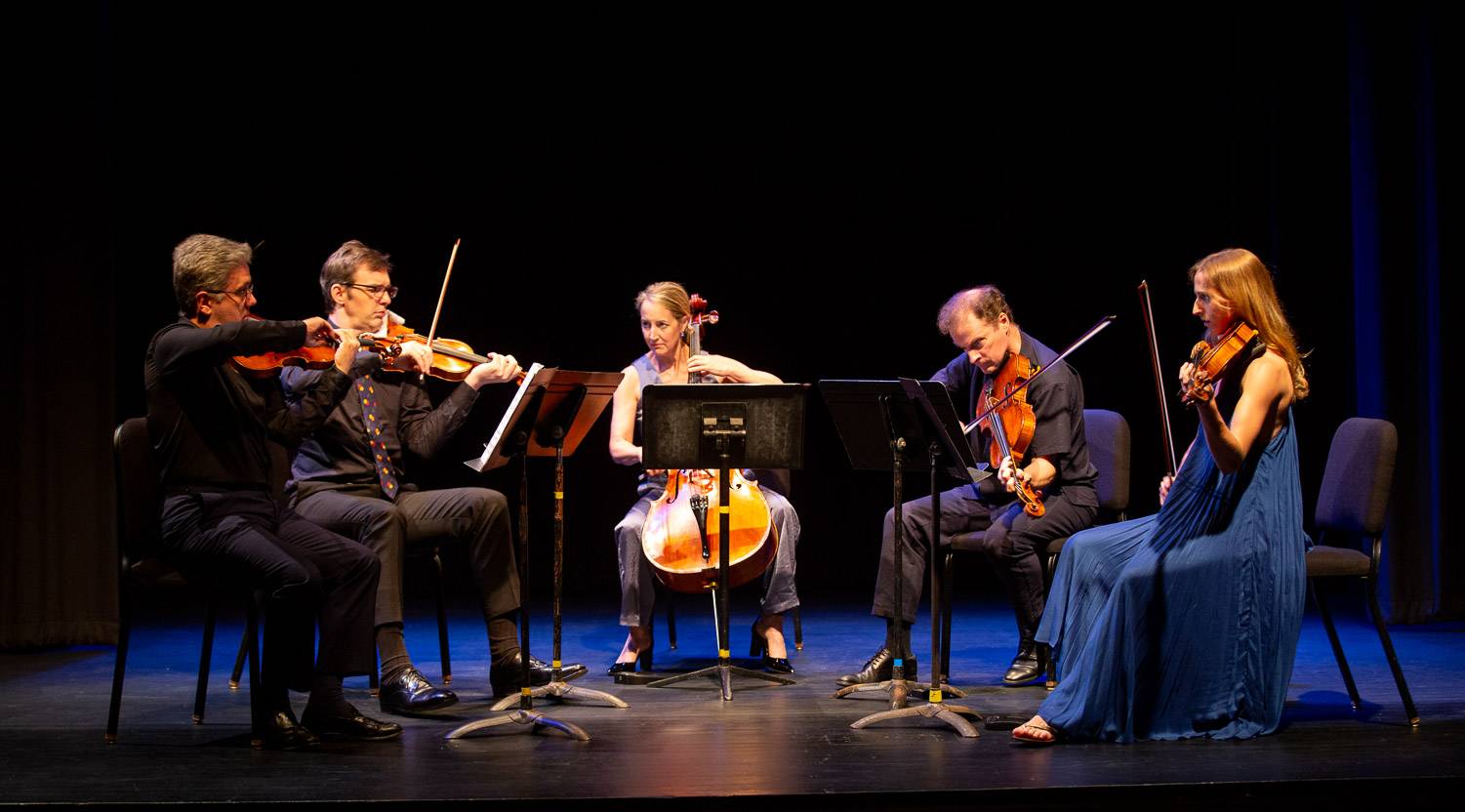 Five orchestral chamber musicians perform in a semi-circle on a black stage