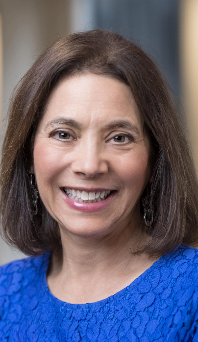 Diana is inside, looking at the camera and smiling. She is wearing a blue shirt.