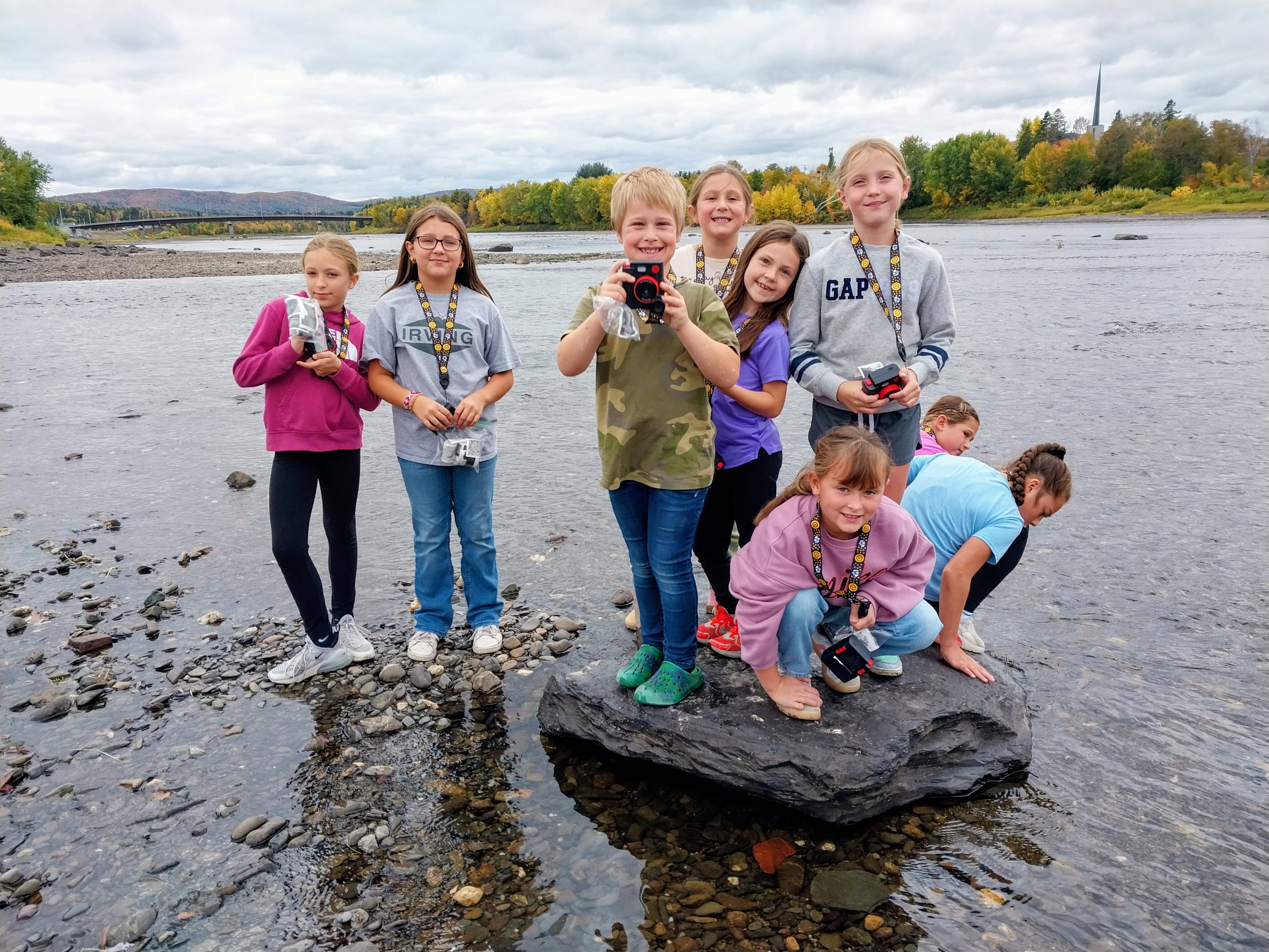 A group of young people take photos outside in shallow water