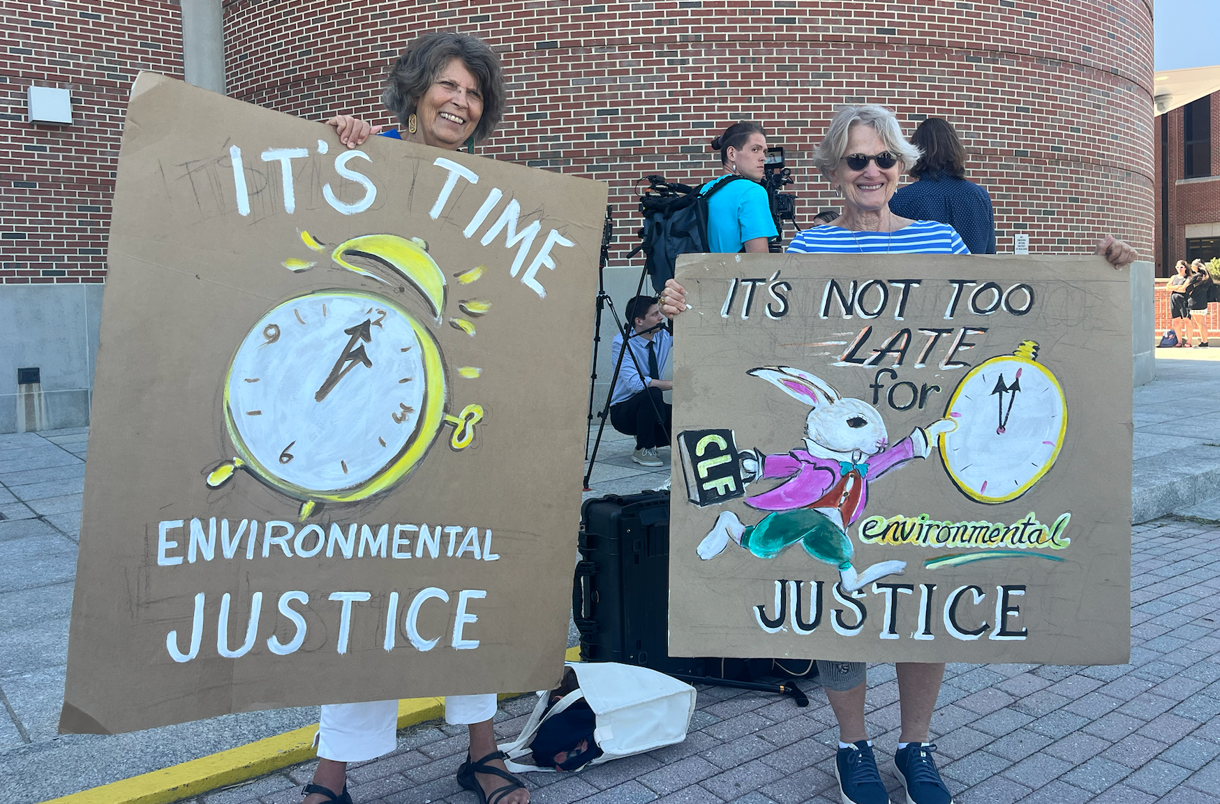Two protesters stand with cardboard signs advocating for environmental justice
