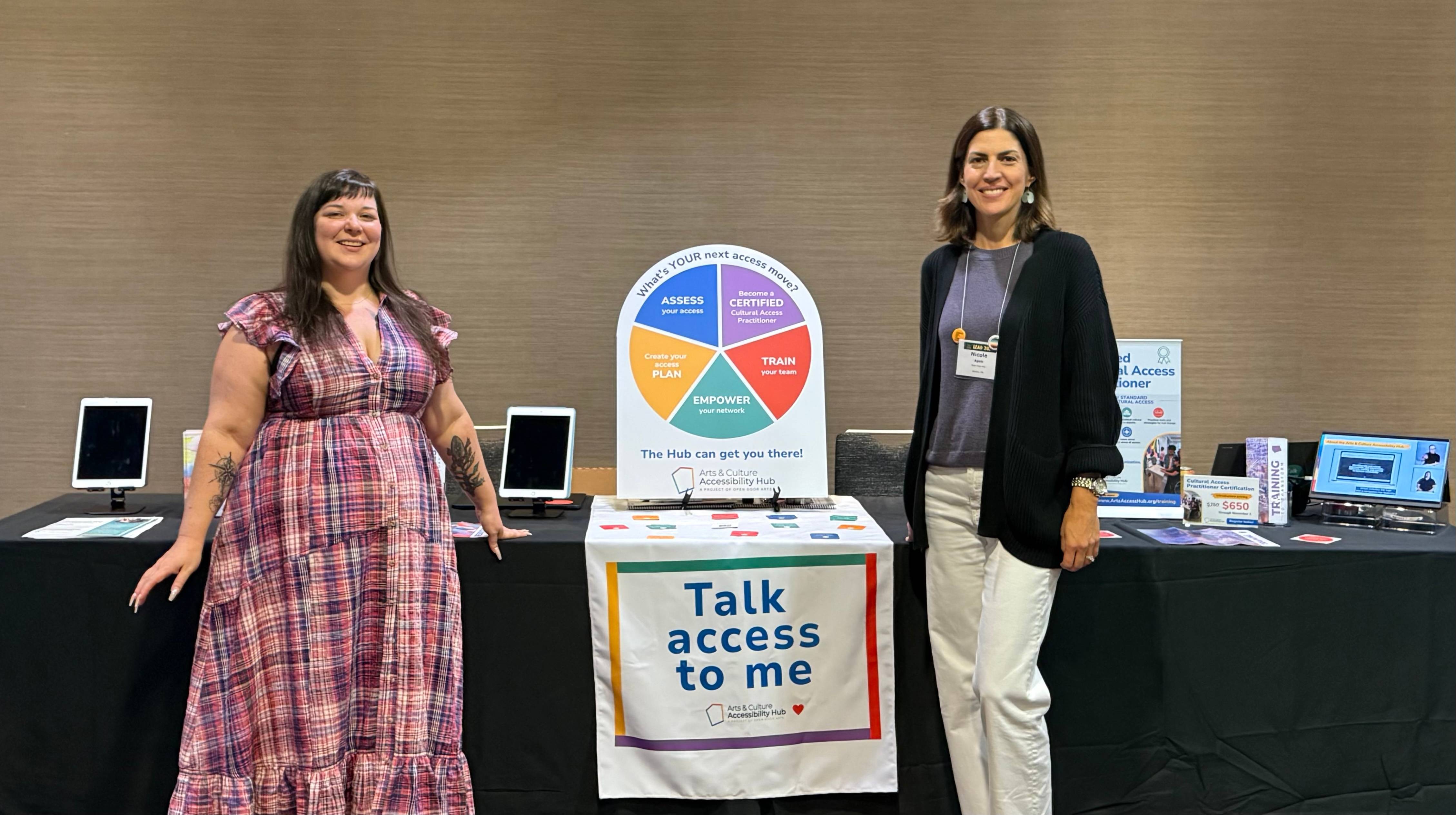 Two people from Open Door Arts stand next to a display about accessibility