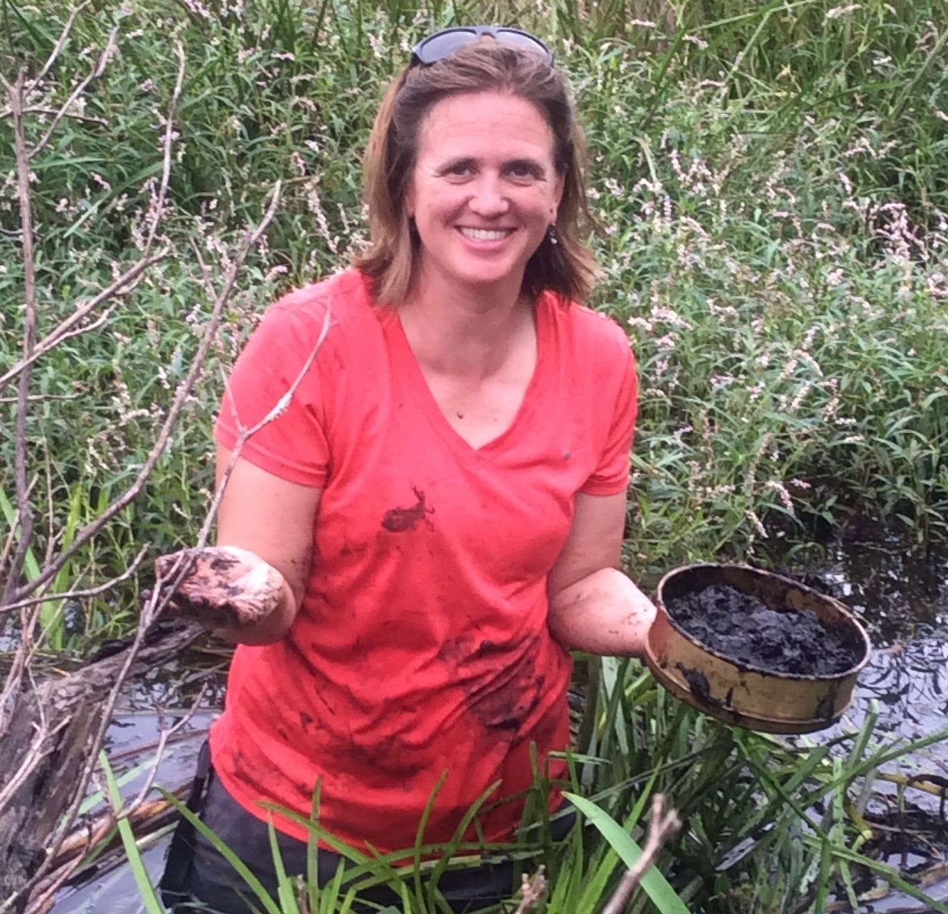 Alene Onion is outside in a marshy area. Her sunglasses are back on top of her head and she is smiling looking at the camera. 