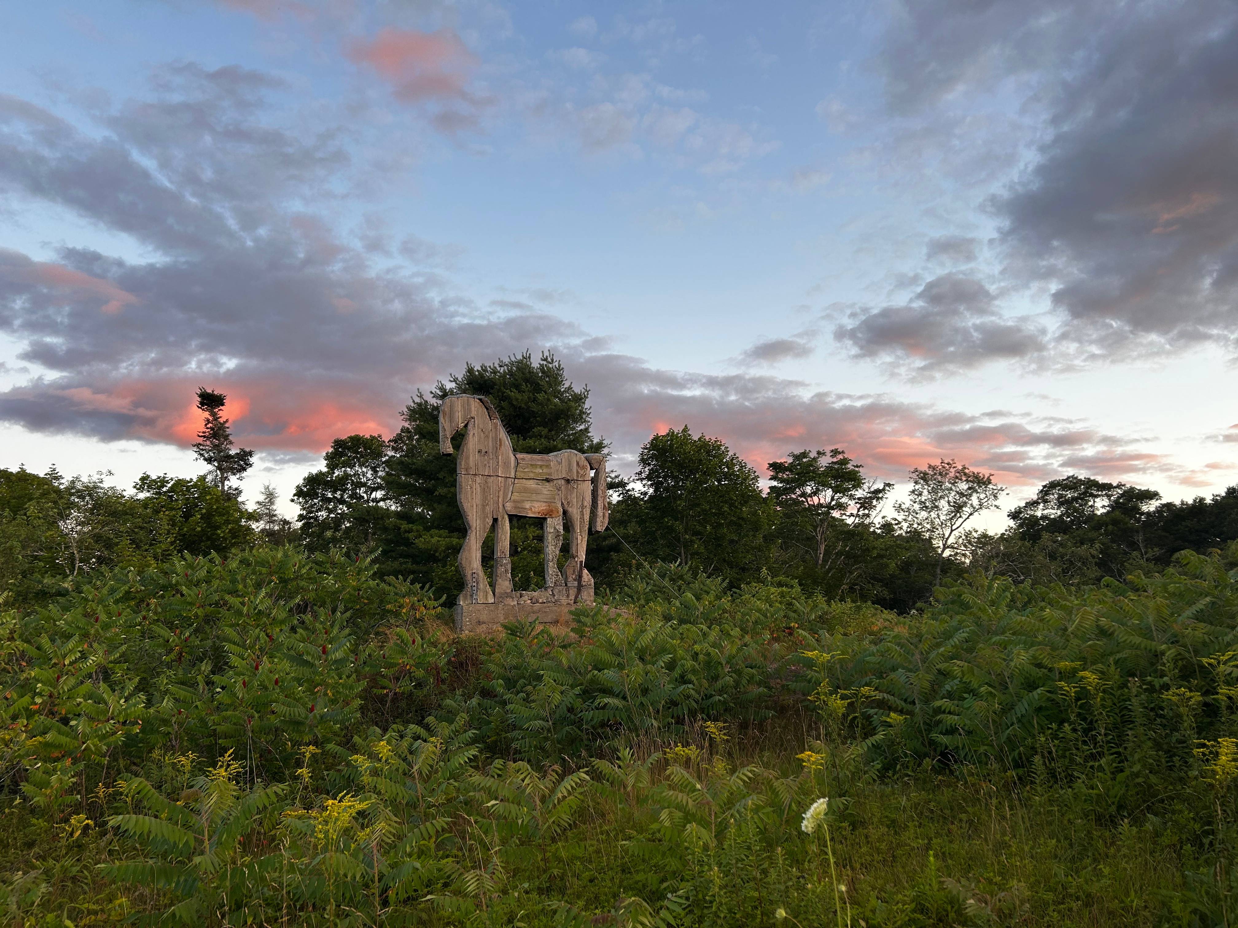 Bernard Langlais's wooden horse sculpture sits on a grassy area against a sunset backdrop