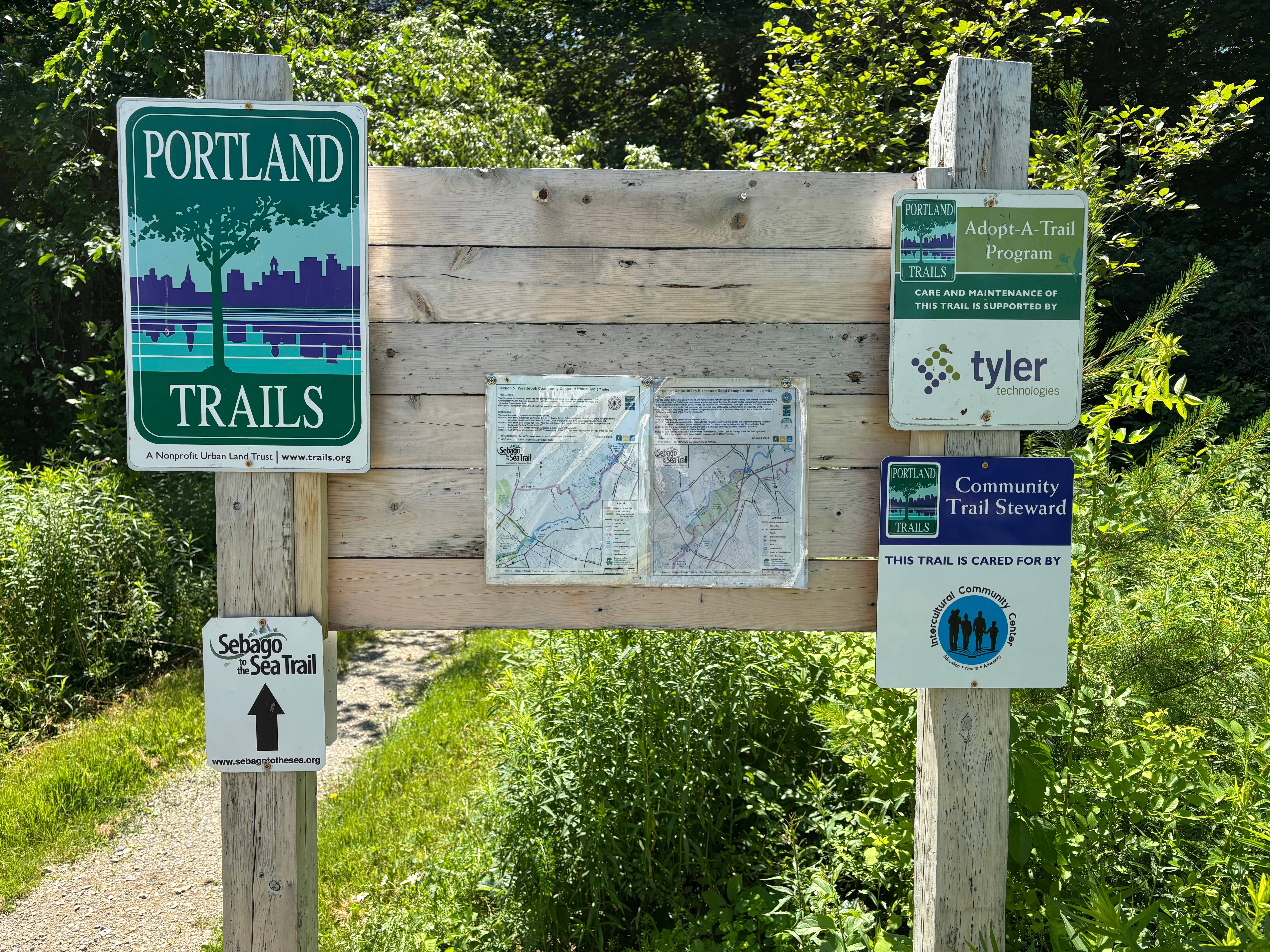 A wooden sign featuring trail-marking signs next to an outdoor trail