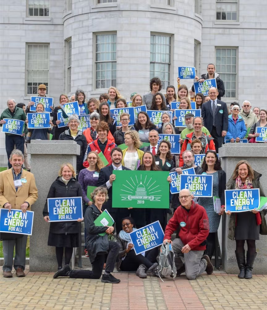 A group of twenty-five or so people holding signs that say 'Clean Energy for All' standing in front of a government building.