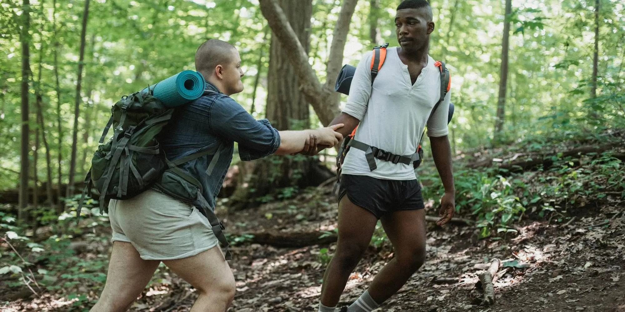 Person wearing a hiking backpack helping another person up a hill
