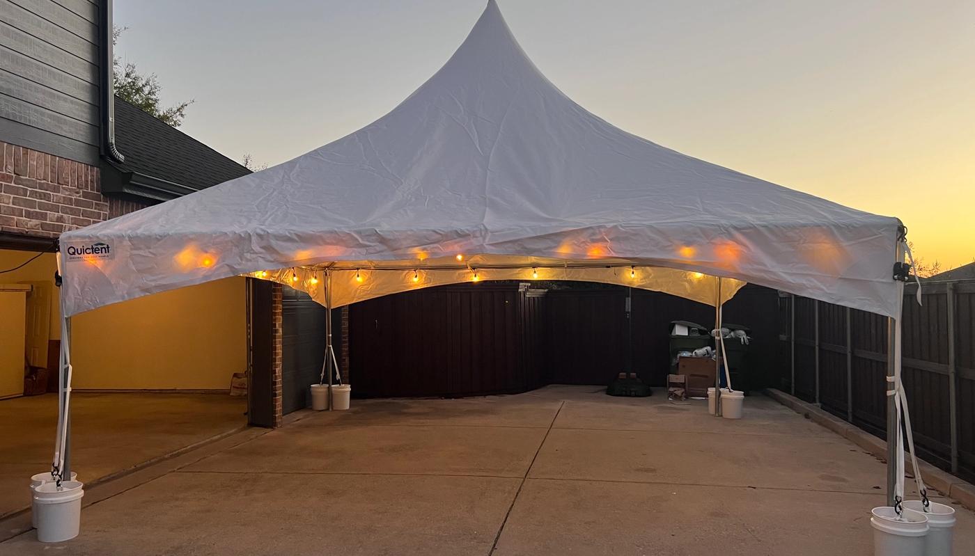 Simply Gathered 20x20 high-peak marquee tent with string lights set up on a driveway at sunset