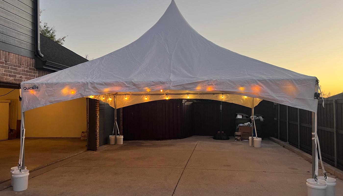 Simply Gathered 20x20 high-peak marquee tent with string lights set up on a driveway at sunset