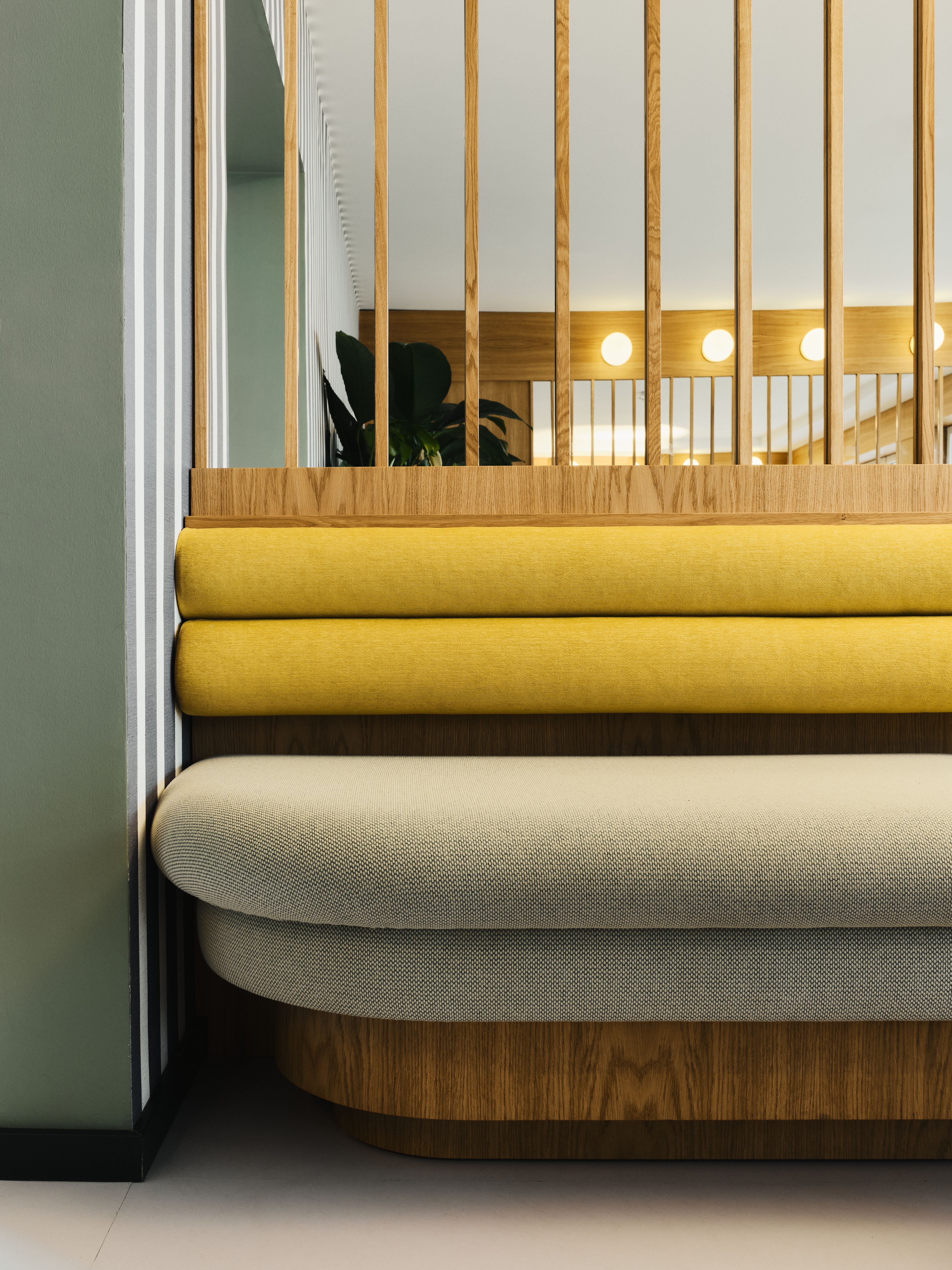 Die weichen Polsterlagen in Gelb und Greige setzen einen grafischen Akzent vor den filigranen Holzlamellen, designed by Stephanie Thatenhorst.