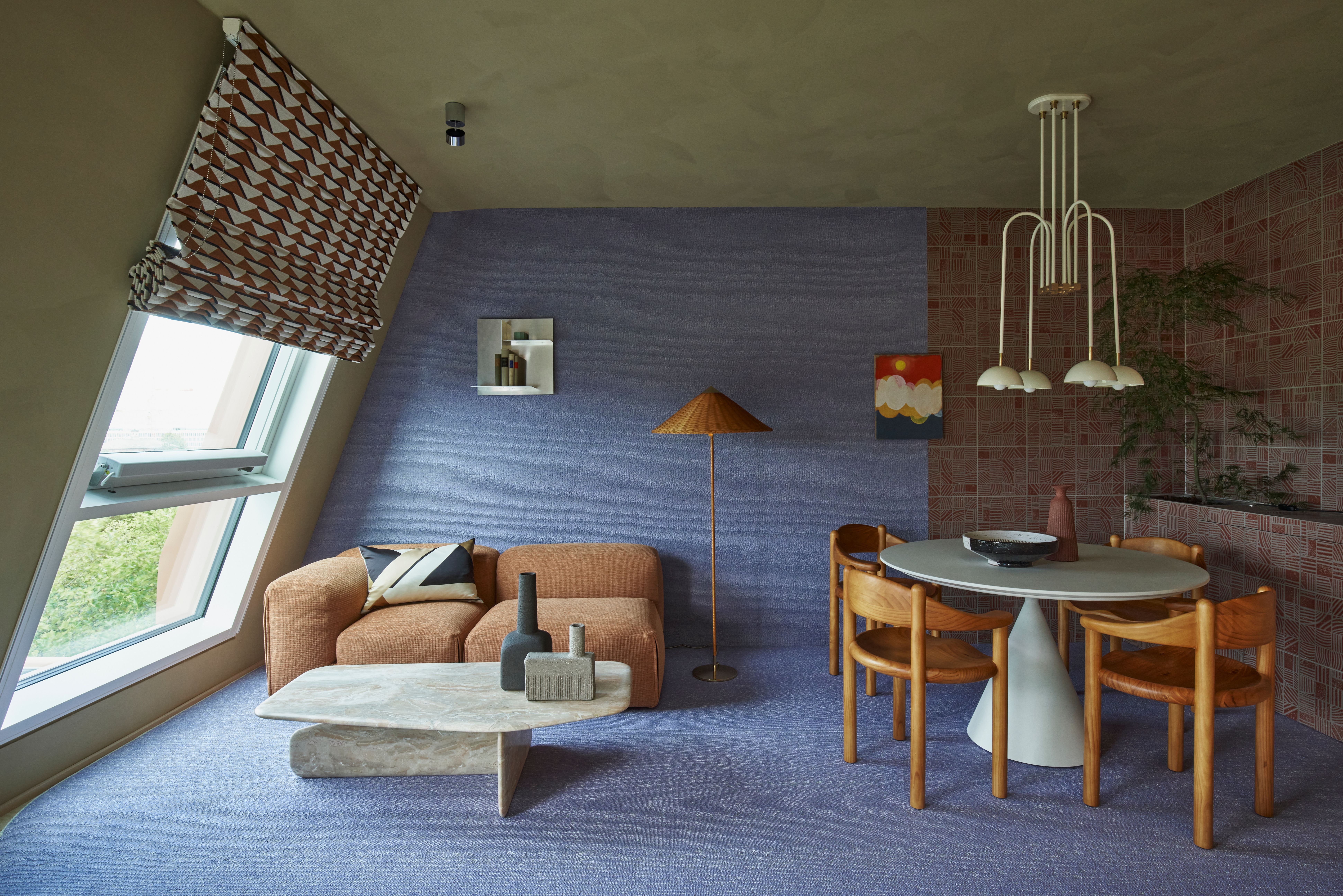 Der Wohnbereich mit orangefarbenem Sofa, Naturstein-Couchtisch und textiler Wandgestaltung wurde von Stephanie Thatenhorst für AD New Perspectives mit einem harmonischen Mix aus Farbe und Materialität gestaltet.