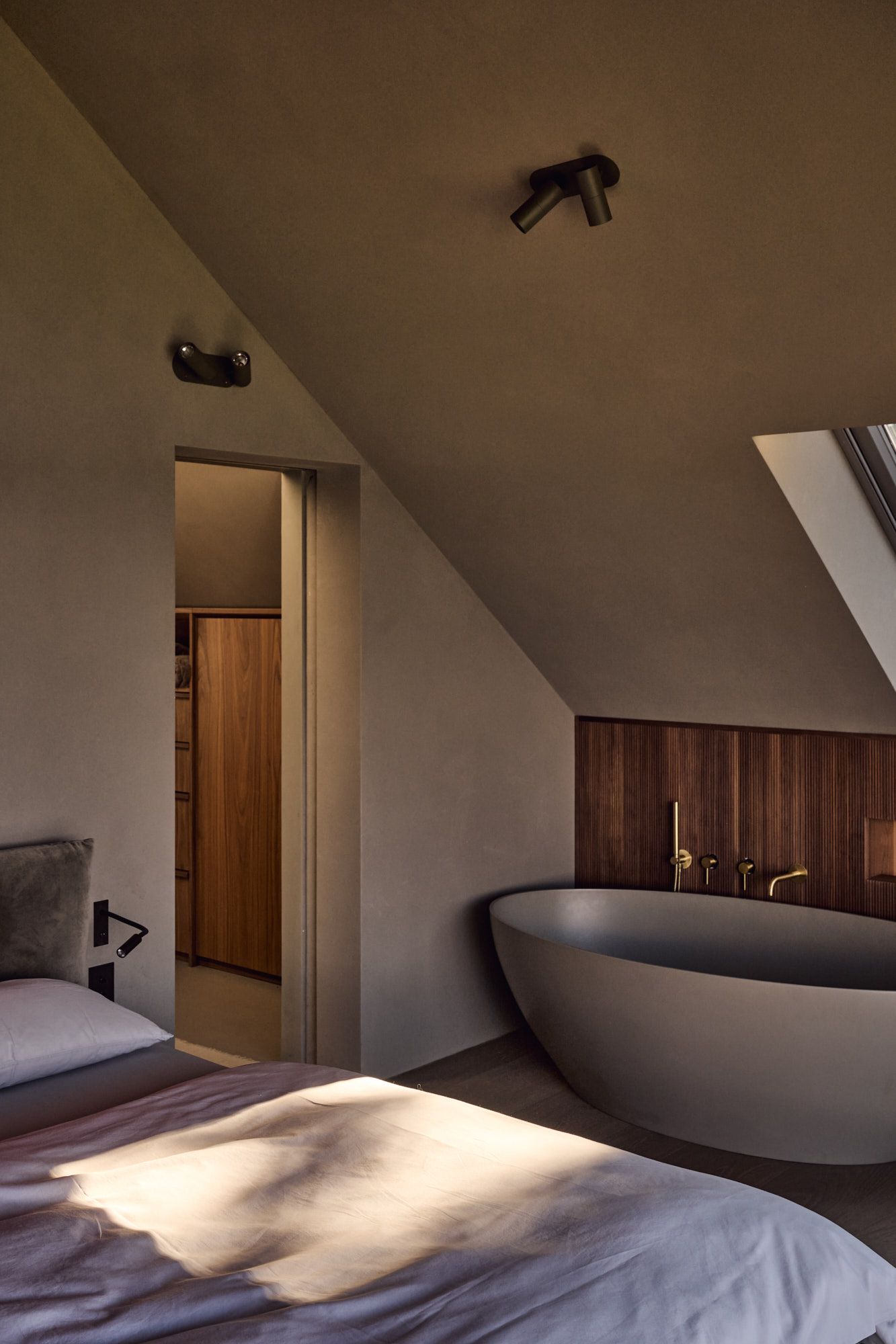 Elegantes Schlafzimmer mit freistehender Badewanne und warmen Naturmaterialien für moderne Wohlfühl-Atmosphäre.