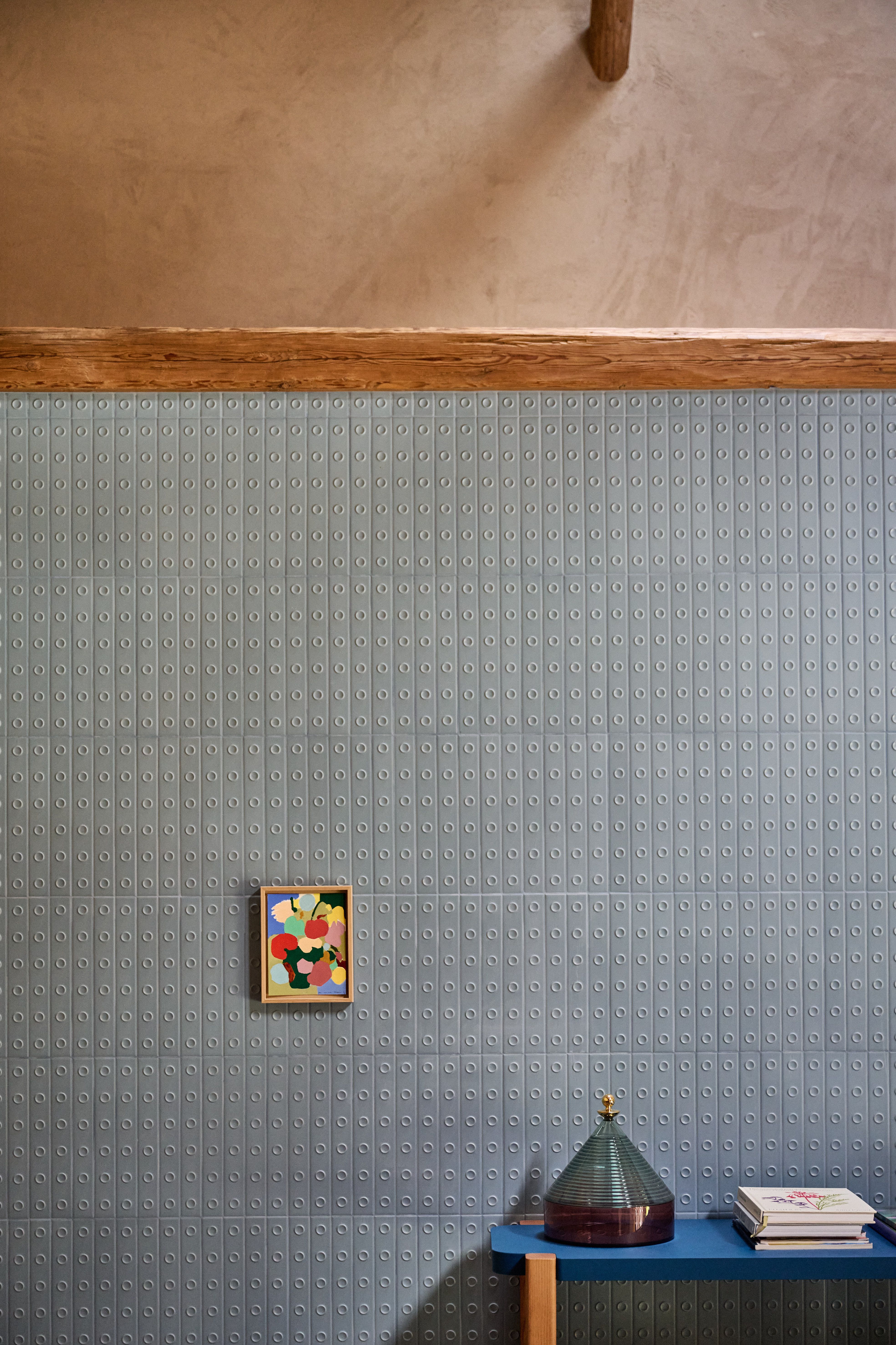 Detailaufnahme einer strukturierten Designwand in gedämpftem Graublau, akzentuiert durch moderne Kunst und minimalistische Dekoration