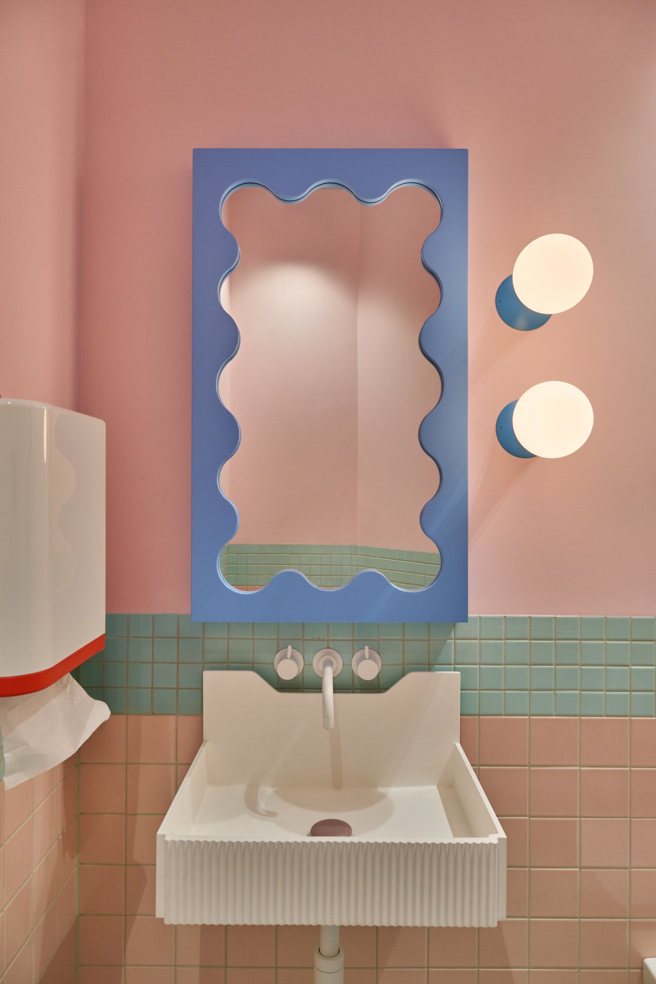 Verspieltes Waschbecken-Design mit pastel­farbenen Fliesen, organischem Spiegelrahmen und moderner Wandbeleuchtung – ein stilvolles Interior-Highlight für kreative Kinder- und Designbäder.