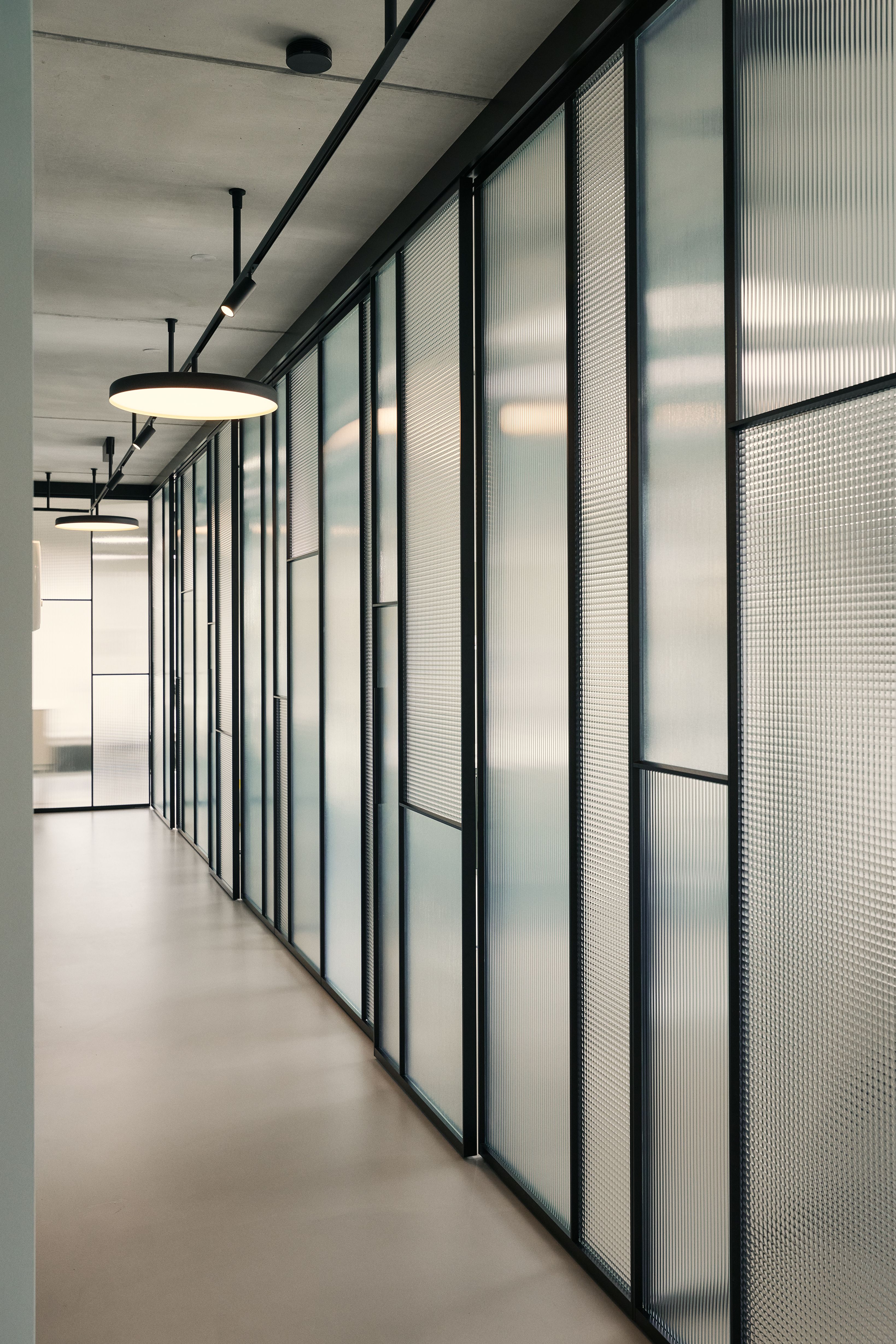 Der lichtdurchflutete Flur mit strukturierten Glasflächen vermittelt in der Zahnarztpraxis Kempten von Stephanie Thatenhorst Transparenz, Ruhe und moderne Orientierung.